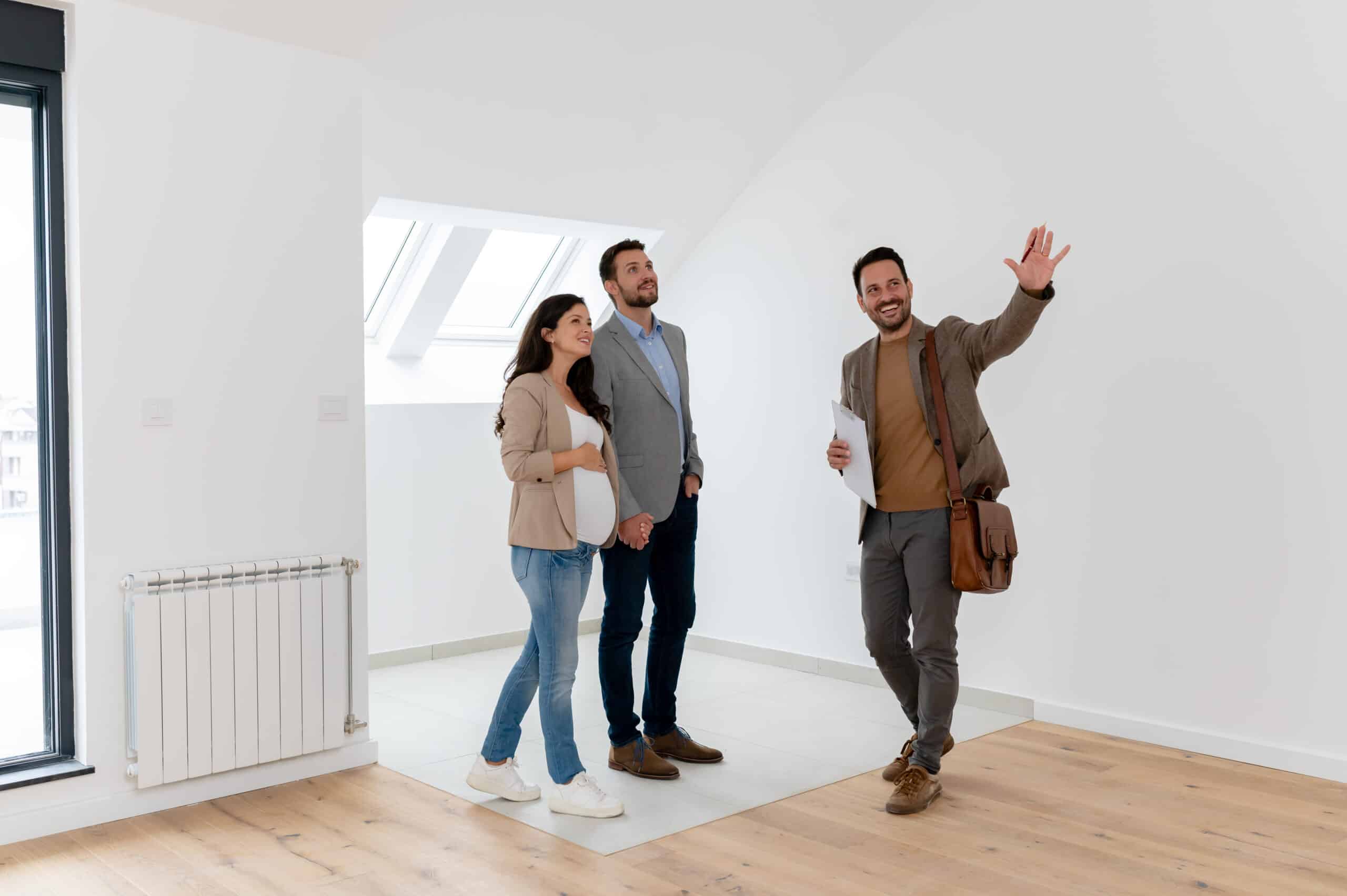 Cheerful couple expecting a baby, talking with a real-estate agent visiting an apartment for sale or for rent.