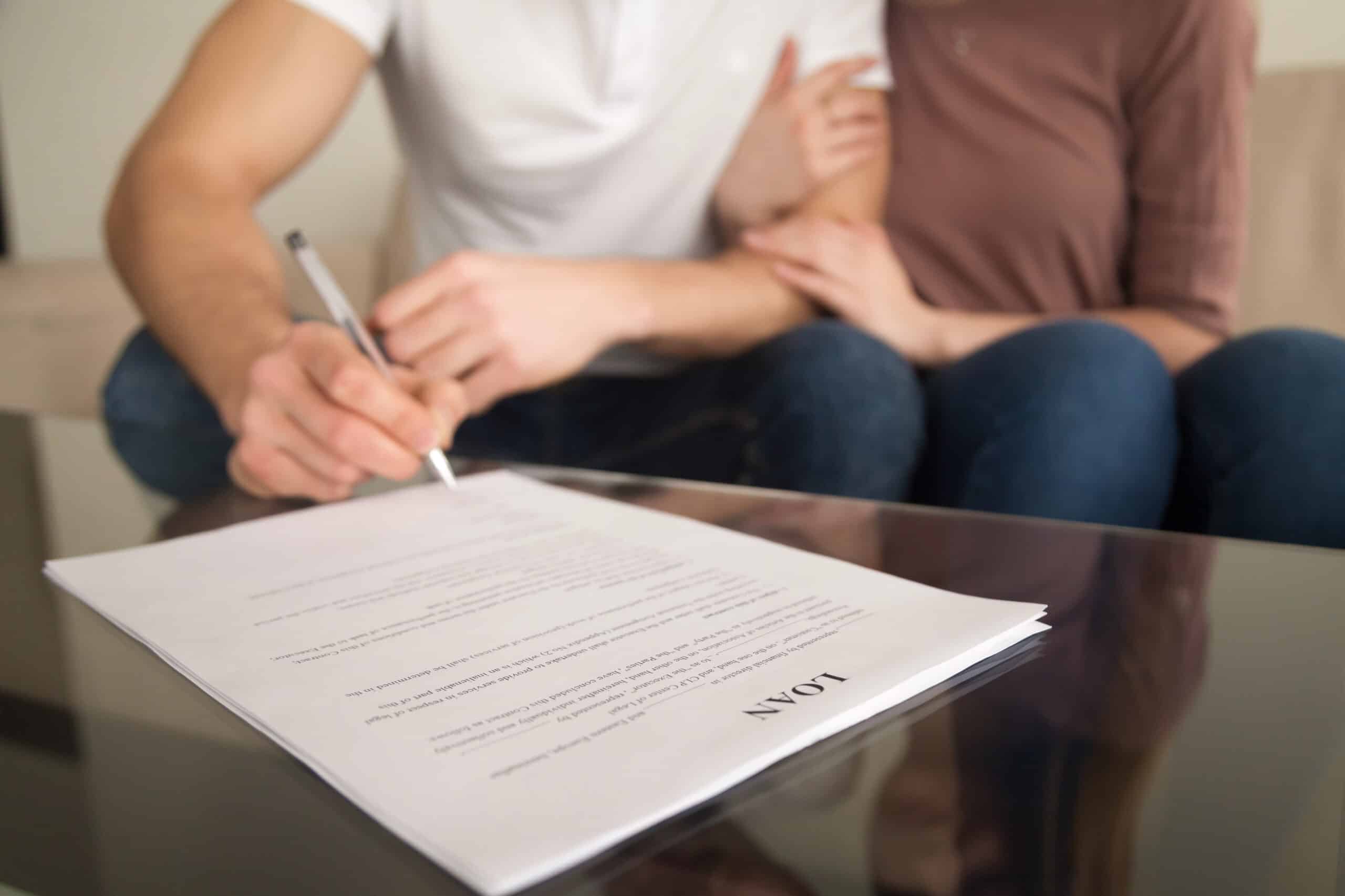 Closeup of couple signing mortgage loan agreement for purchasing property