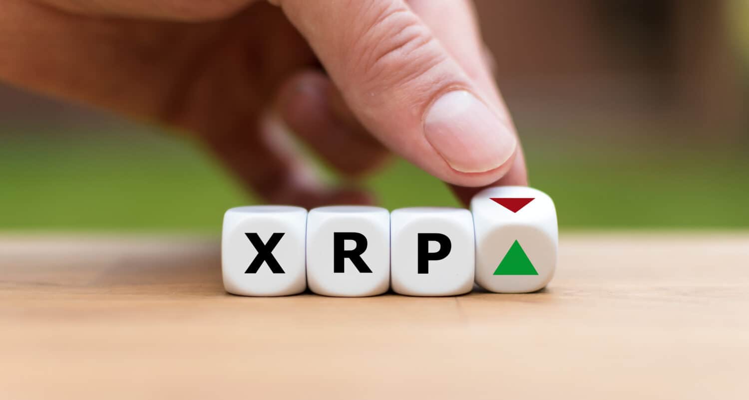 Hand is turning a dice and changes the direction of an arrow symbolizing that the value of the crypto currency Ripple (XRP) is going up (or vice versa)