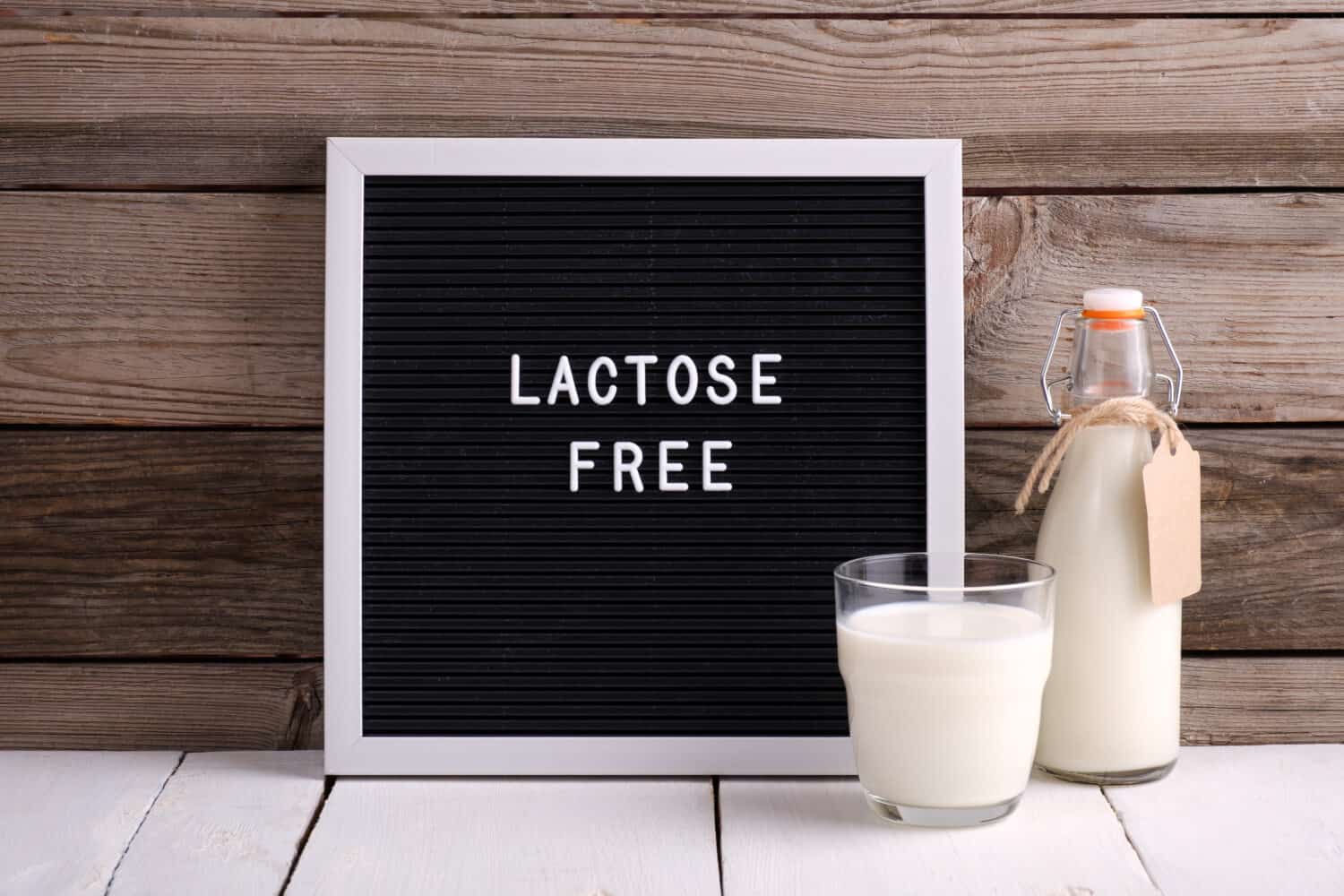 Allergic food concept. Milk bottle, milk glass and letter board with text LACTOSE FREE on wooden background.
