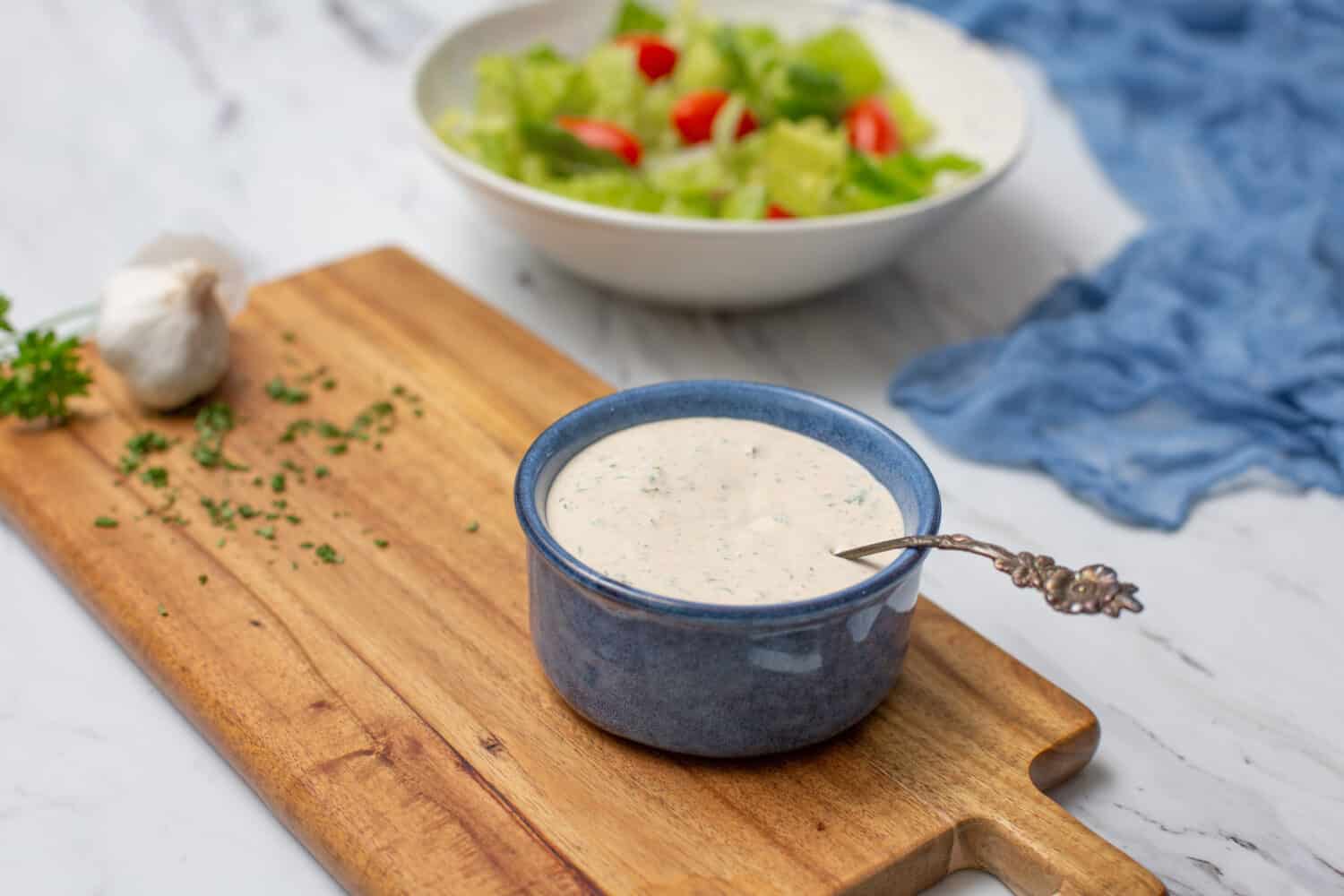 Homemade Buttermilk Ranch Dressing in Blue Bowl on White Countertop; Prepared Salad in Background