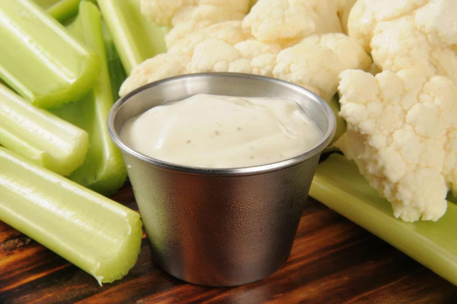 Closeup of celery sticks and cauliflower with a serving dish of ranch dressing dip