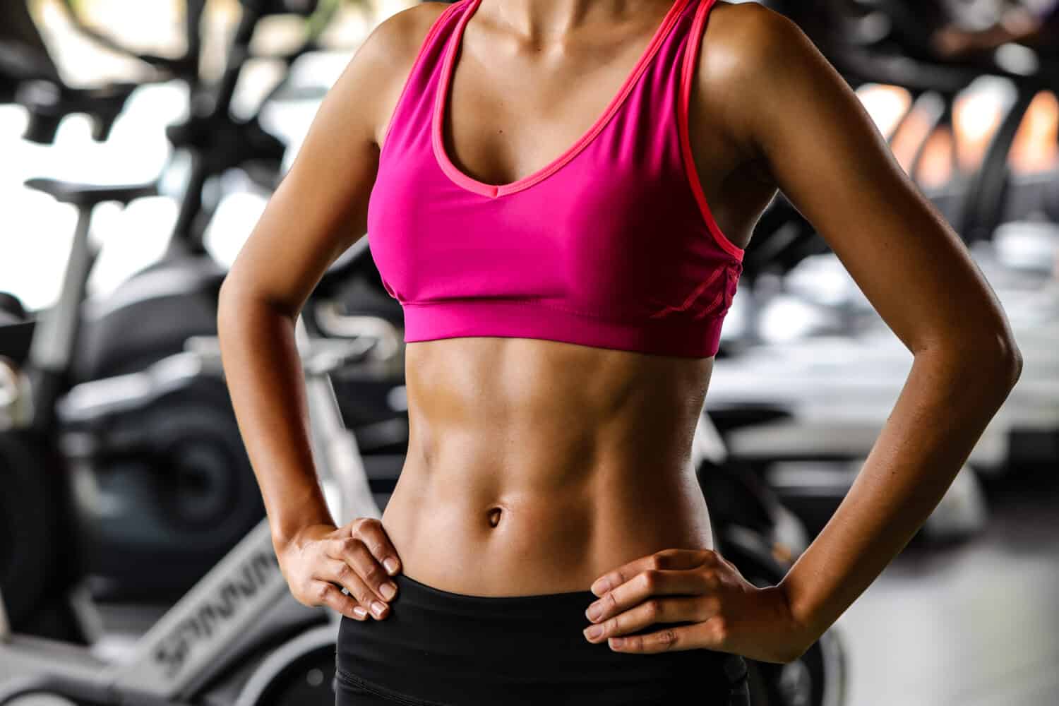 Close-up of a woman's body bodybuilder in the gym. Portrait of muscular woman showing Strong abs on professinal gym background. Beautiful abdominal muscle.