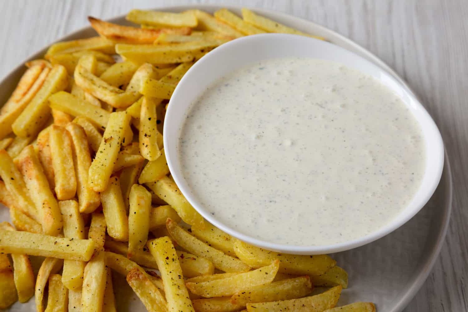 Homemade Crispy Ranch Fries on a gray plate on a white wooden table, side view. Close-up.