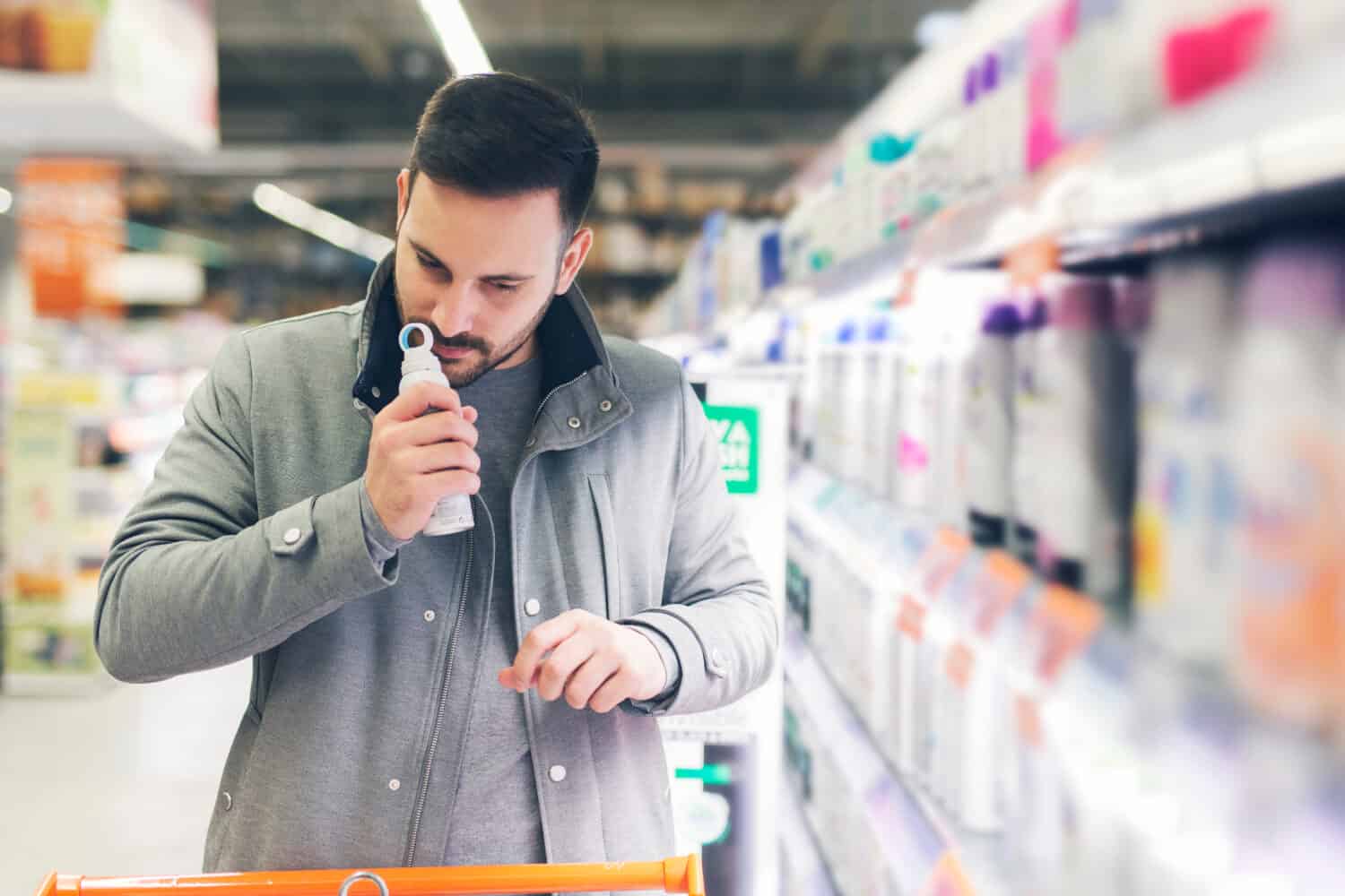 Young attractive man in grey coat do shopping in the supermarket
