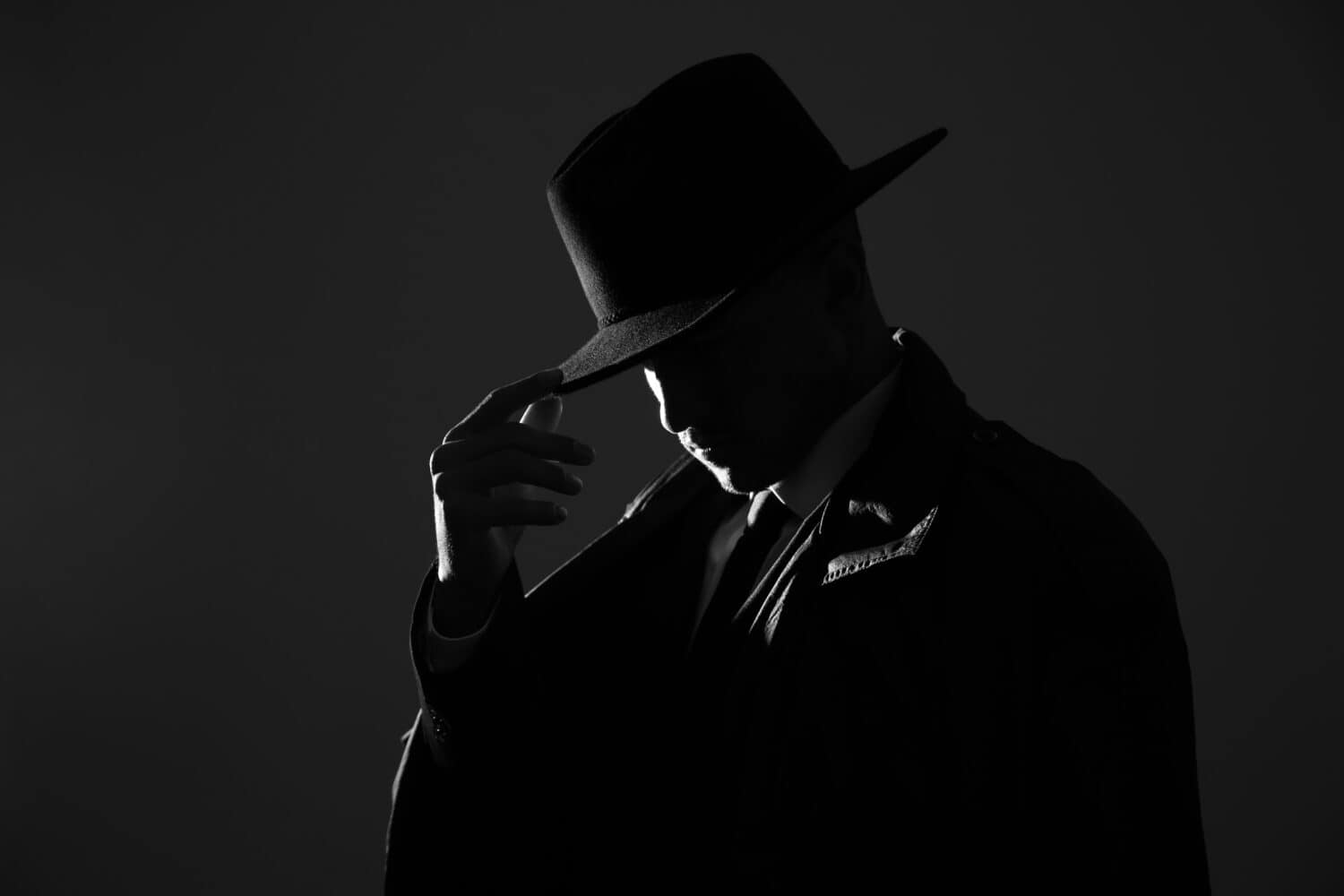 Old fashioned detective in hat on dark background, black and white effect