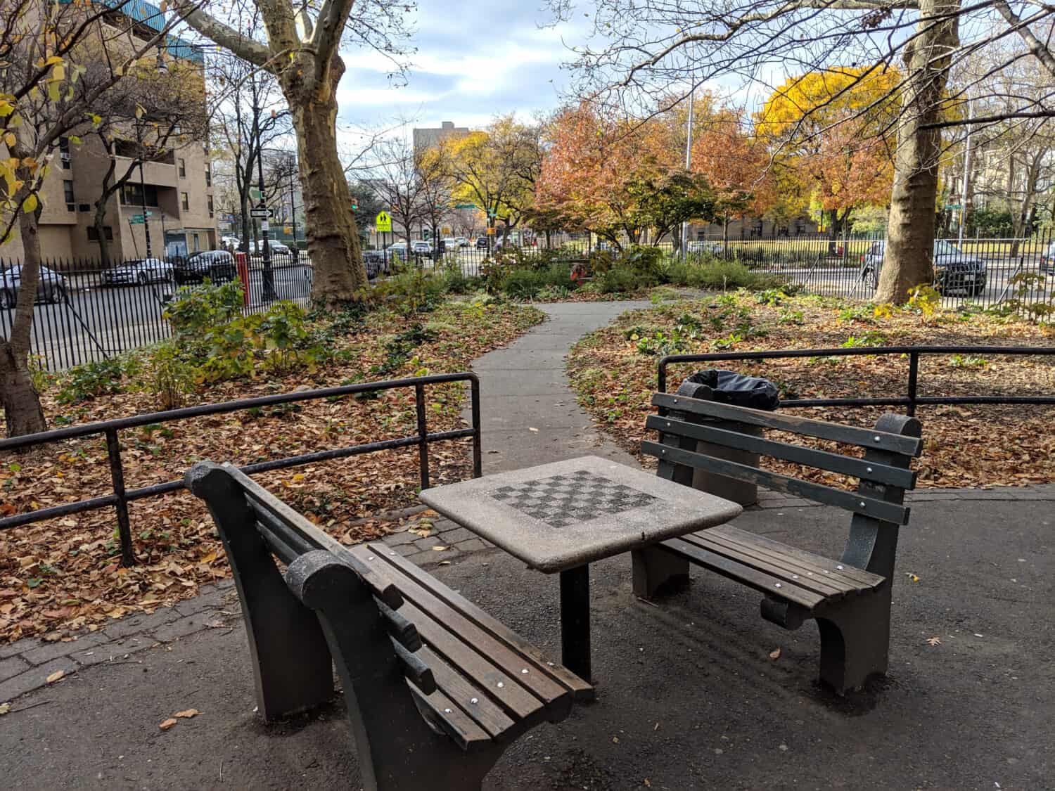 Empty benches with an empty chess table in an empty park with fall foliage in Stuyvesant Heights in Brooklyn