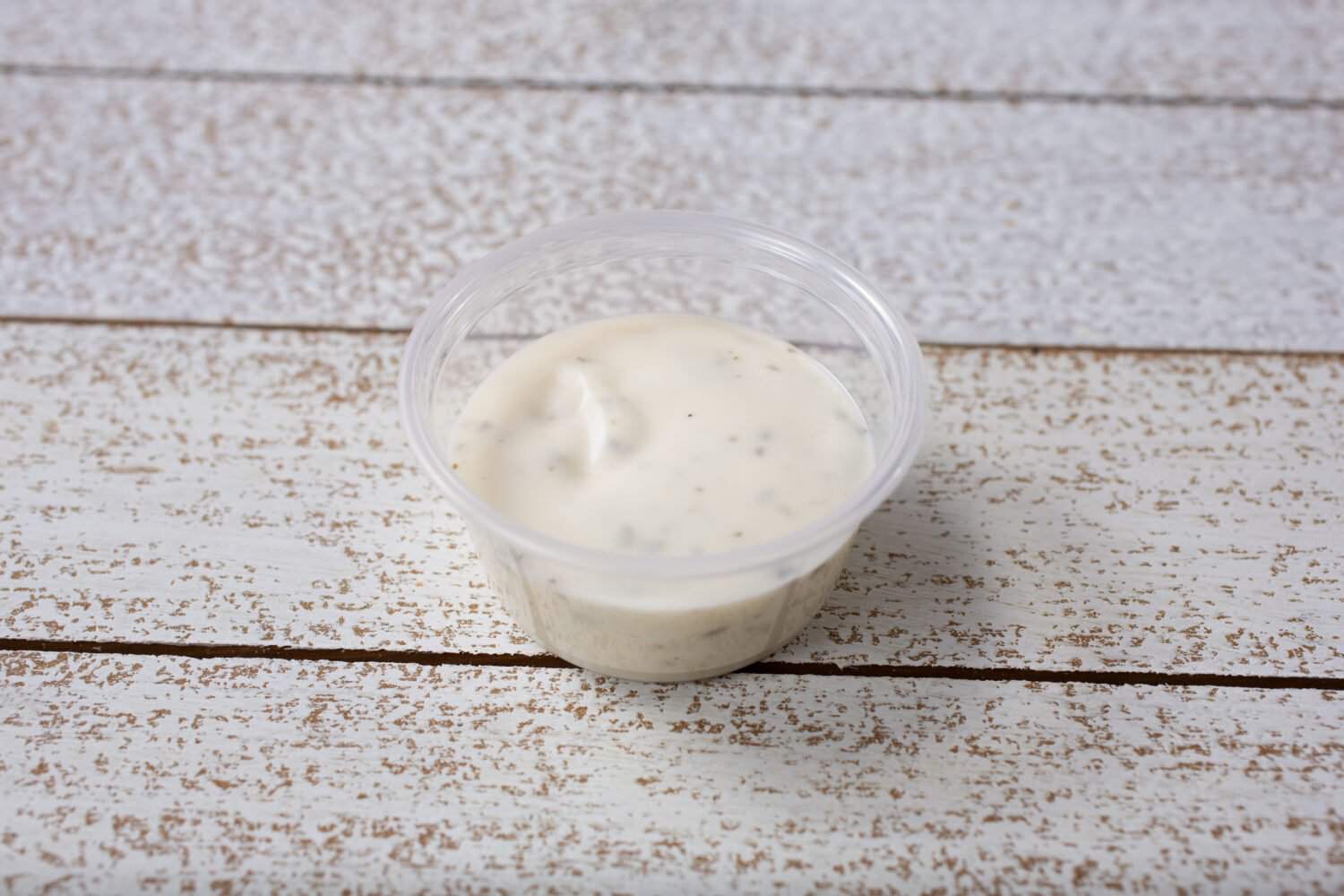 A view of ranch dressing in a small plastic condiment cup.