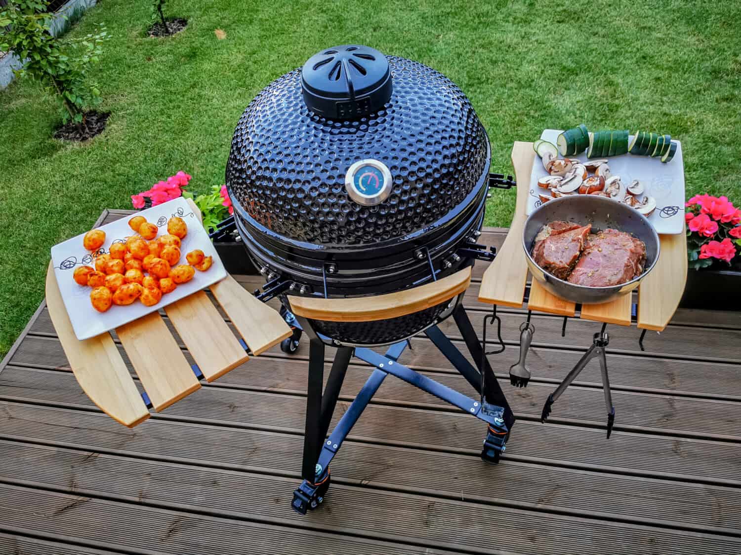 A kamado egg type barbeque grill standing on a living house terrace with beef steaks and vegetables to be cooked.