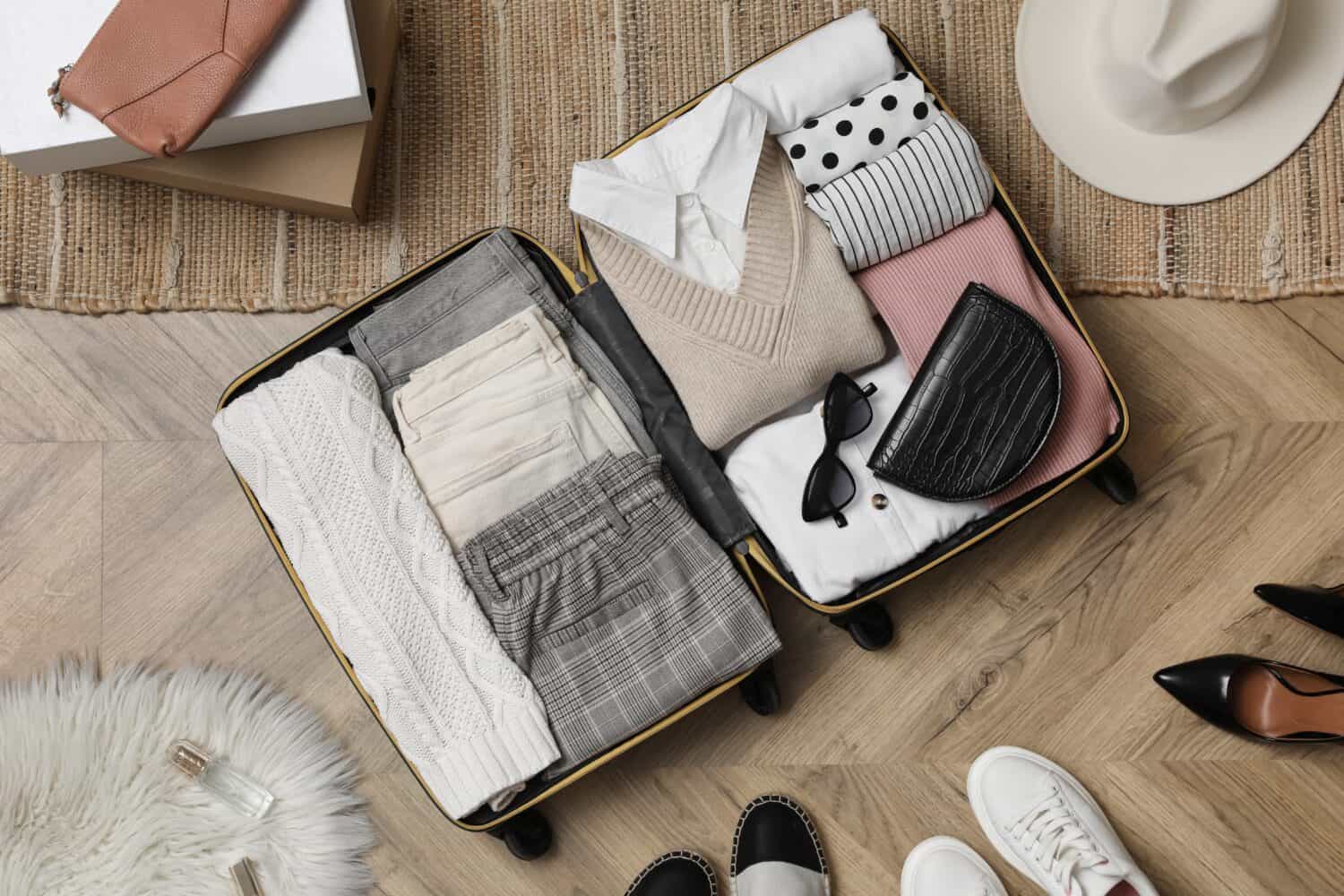 Open suitcase with folded clothes, accessories and shoes on floor, flat lay