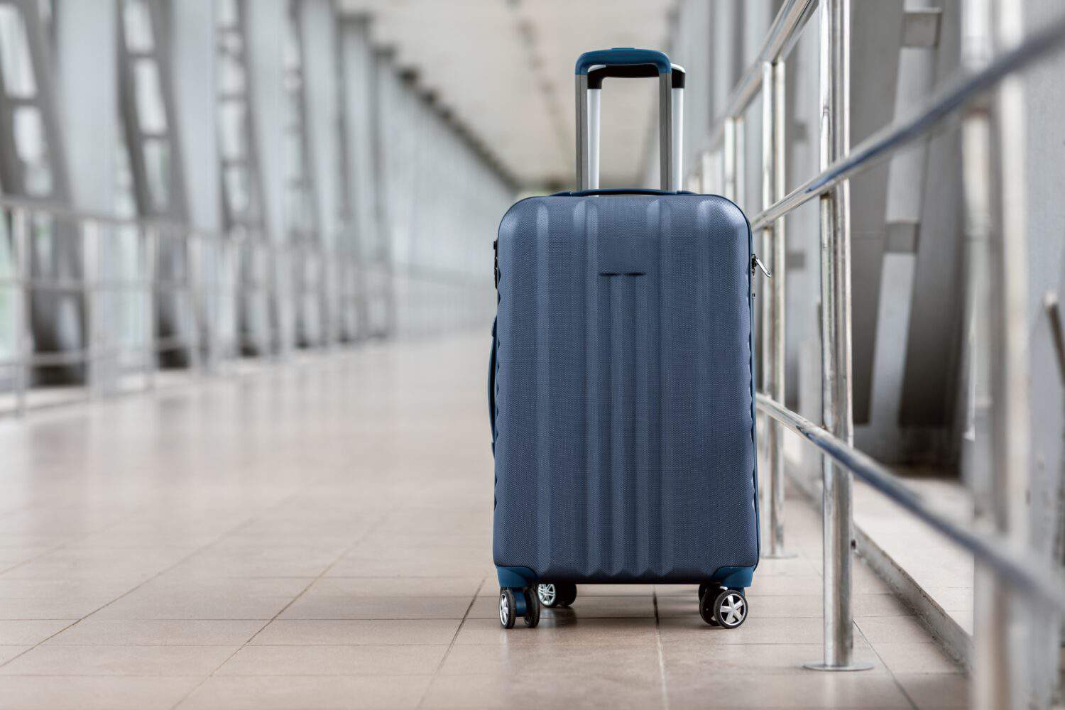 Closeup Shot Of Stylish Cabin Baggage Suitcase Standing In Empty Airport Hall, Blue Hand Luggage Bag Waiting At Terminal, Advertisement Banner For Air Travels And Flight Bookings, Copy Space