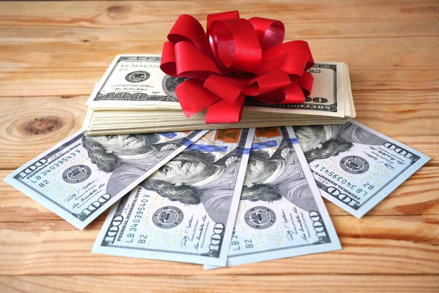 stack of american dpllars cash money and red bow background, money gift concept, closeup