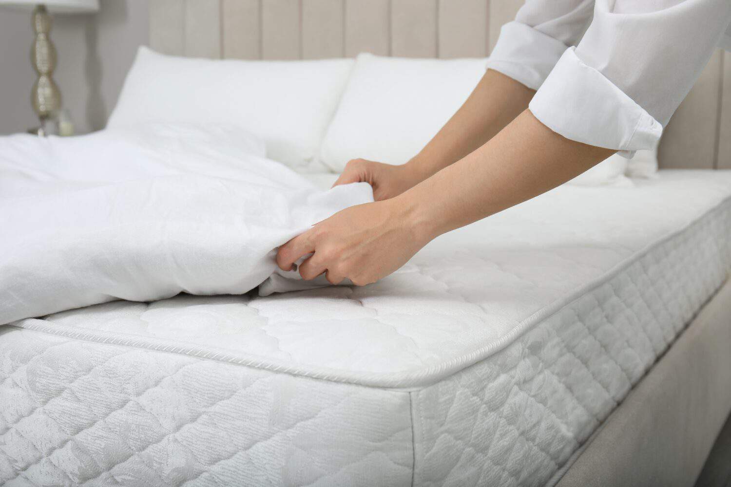 Woman putting blanket over soft white mattress on bed indoors, closeup