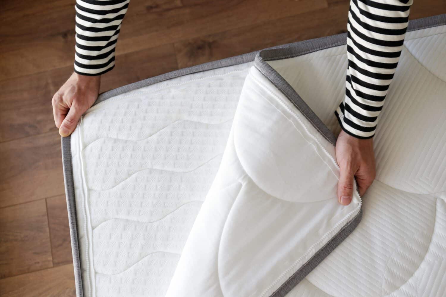 Cropped shot of man showcasing the waterproof topper for white orthopedic mattress. Male unzipping hypoallergenic foam matress protector. Close up, copy space, top view, background.