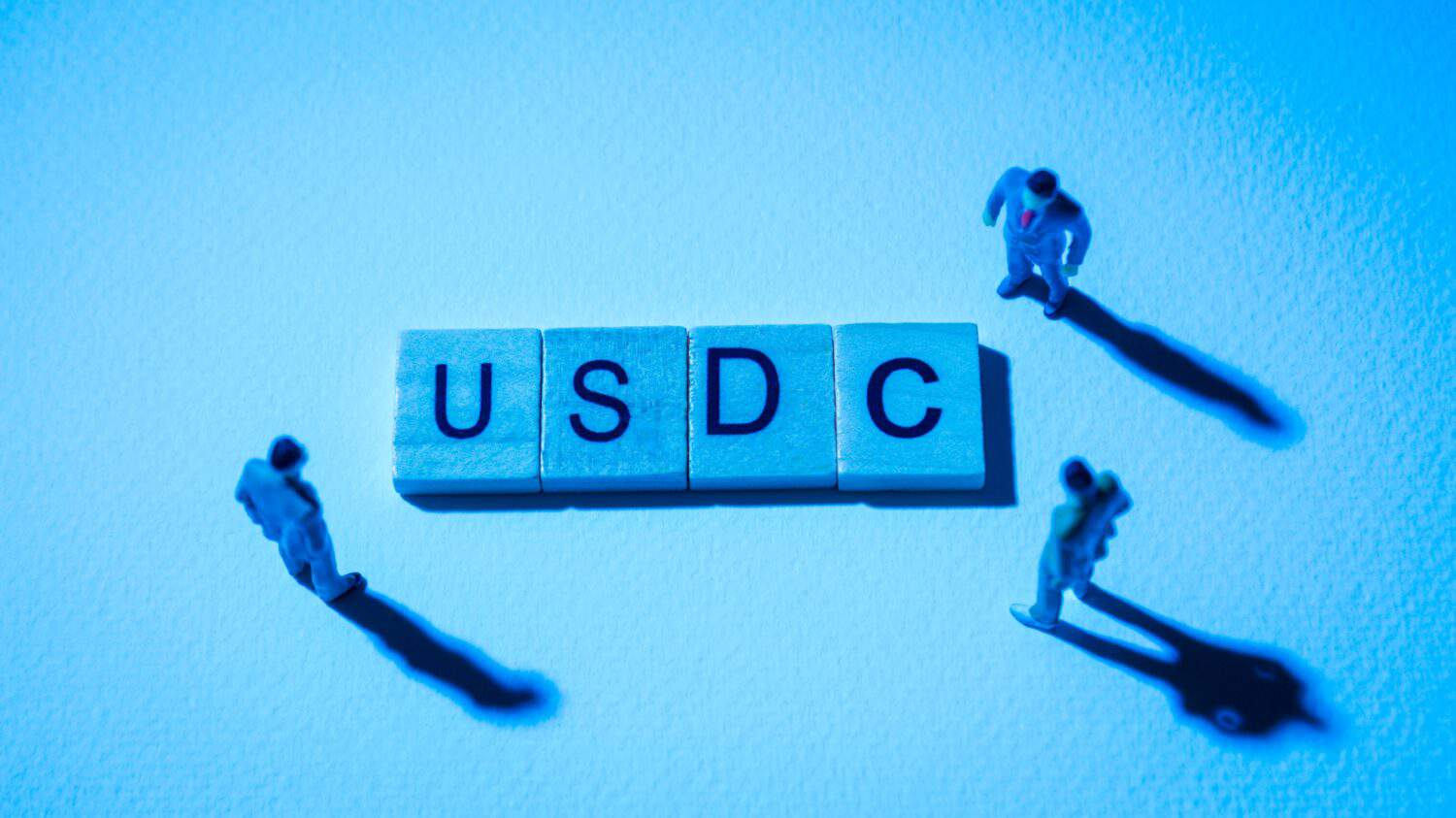 Miniature figures businessman : meeting on USDC word by wooden block words on white paper background in blue light, USDC or USD Coin in concept of digital money, cryptocurrency and business.