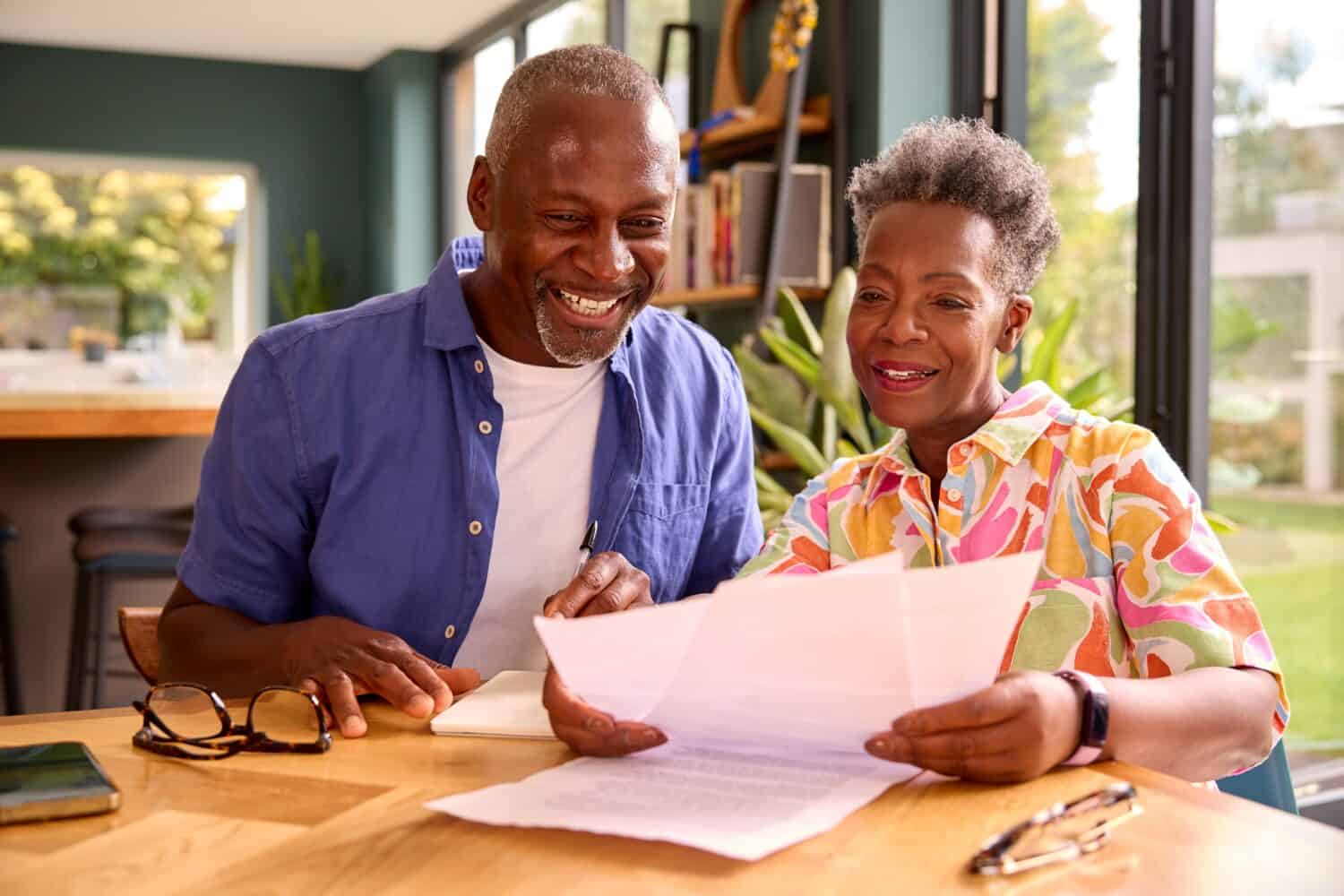 Smiling Senior Couple Sitting Around Table At Home Reviewing Finances