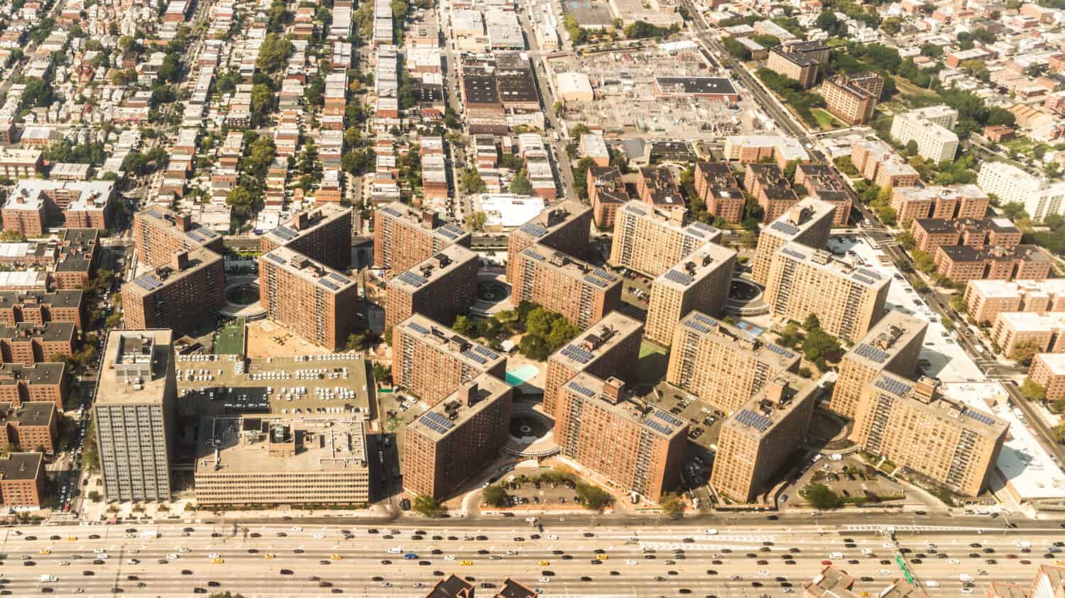 Aerial view of the Borough of Queens, New York, showing geometrically arranged and densely packed buildings and a multi-lane super highway
