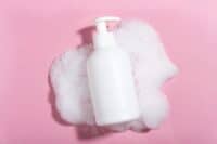 Cosmetics for face, body and hair care. Moisturizer, shampoo or facial cleanser on pink background with foam
