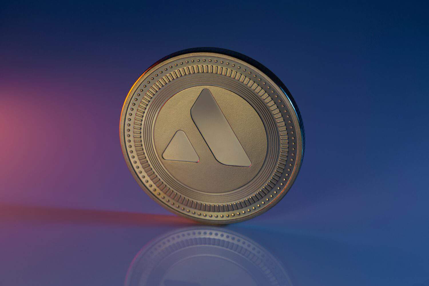 Avalanche AVAX Cryptocurrency Physical Coin Placed on reflective surface and lit with orange and blue lights.