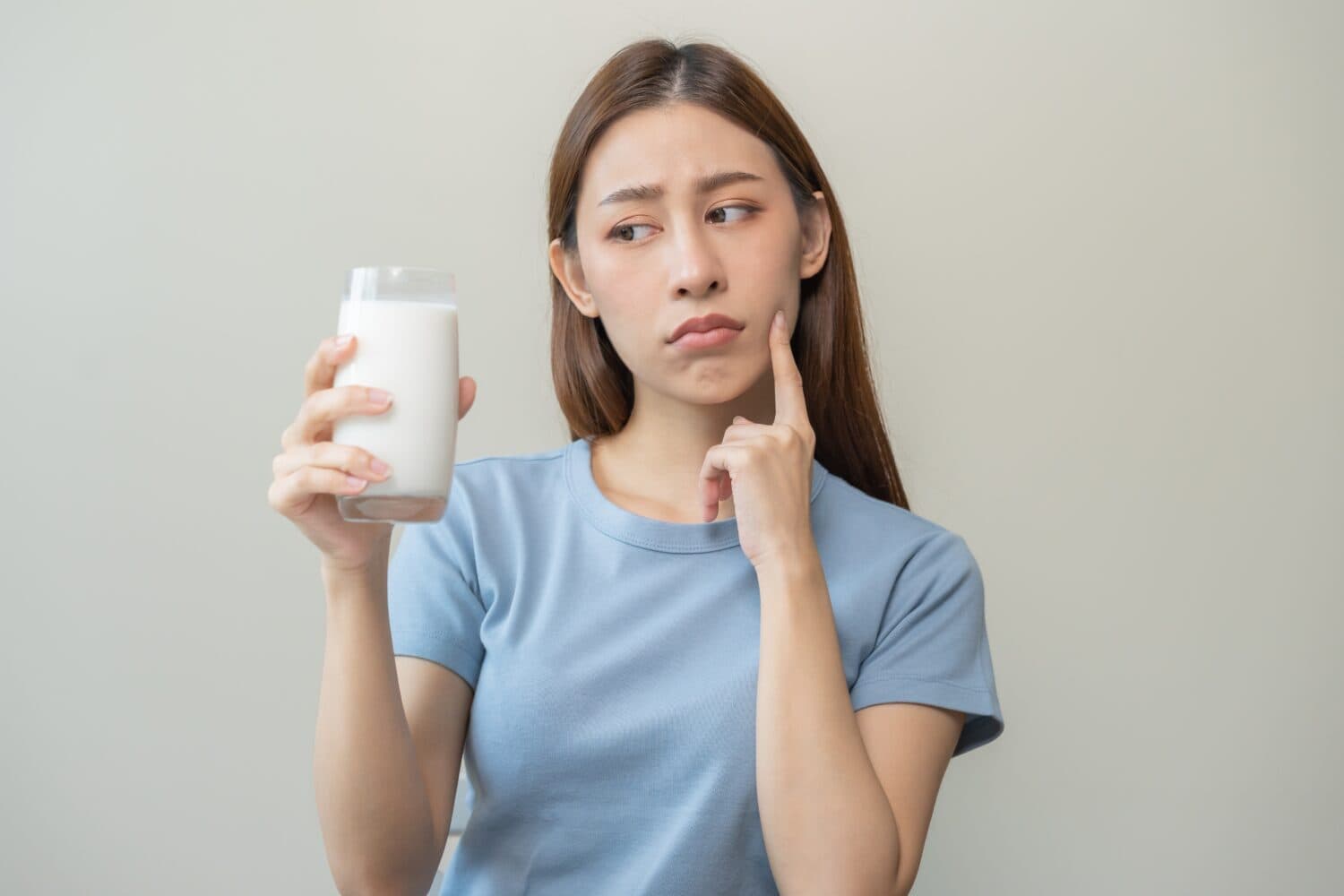 Allergy asian young woman, girl looking, holding glass of milk, face in thinking before drink milk as it may upset her stomach ache, pain. Lactose intolerance and dairy food , health problem concept.