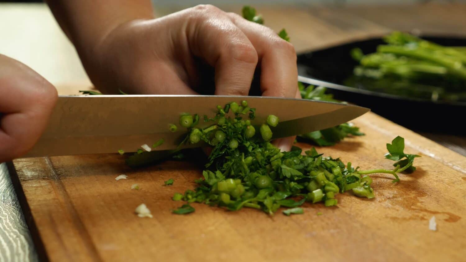 Close-up of a chef's hands with a knife slicing parsley on a cutting board. Side view. Delicious and healthy food