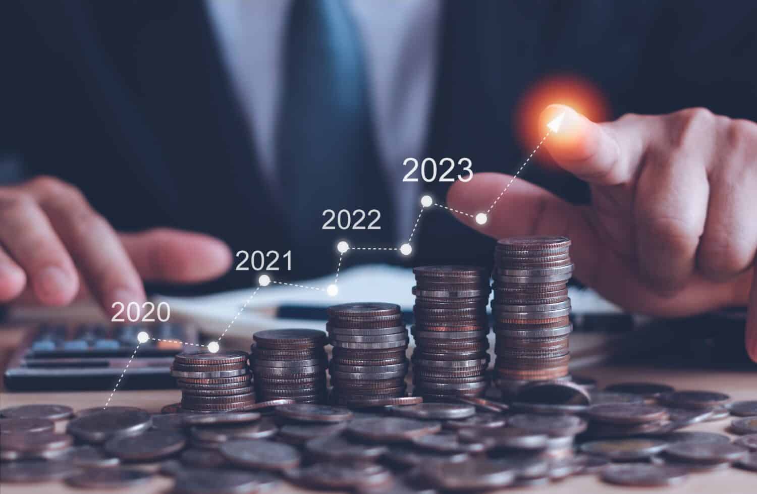Businessman touch arrow showing financial growth 2023 on stacked coins business background,Concepts savings money and accounting, investments, banks, bonds, dividends, inflation and digital assets.