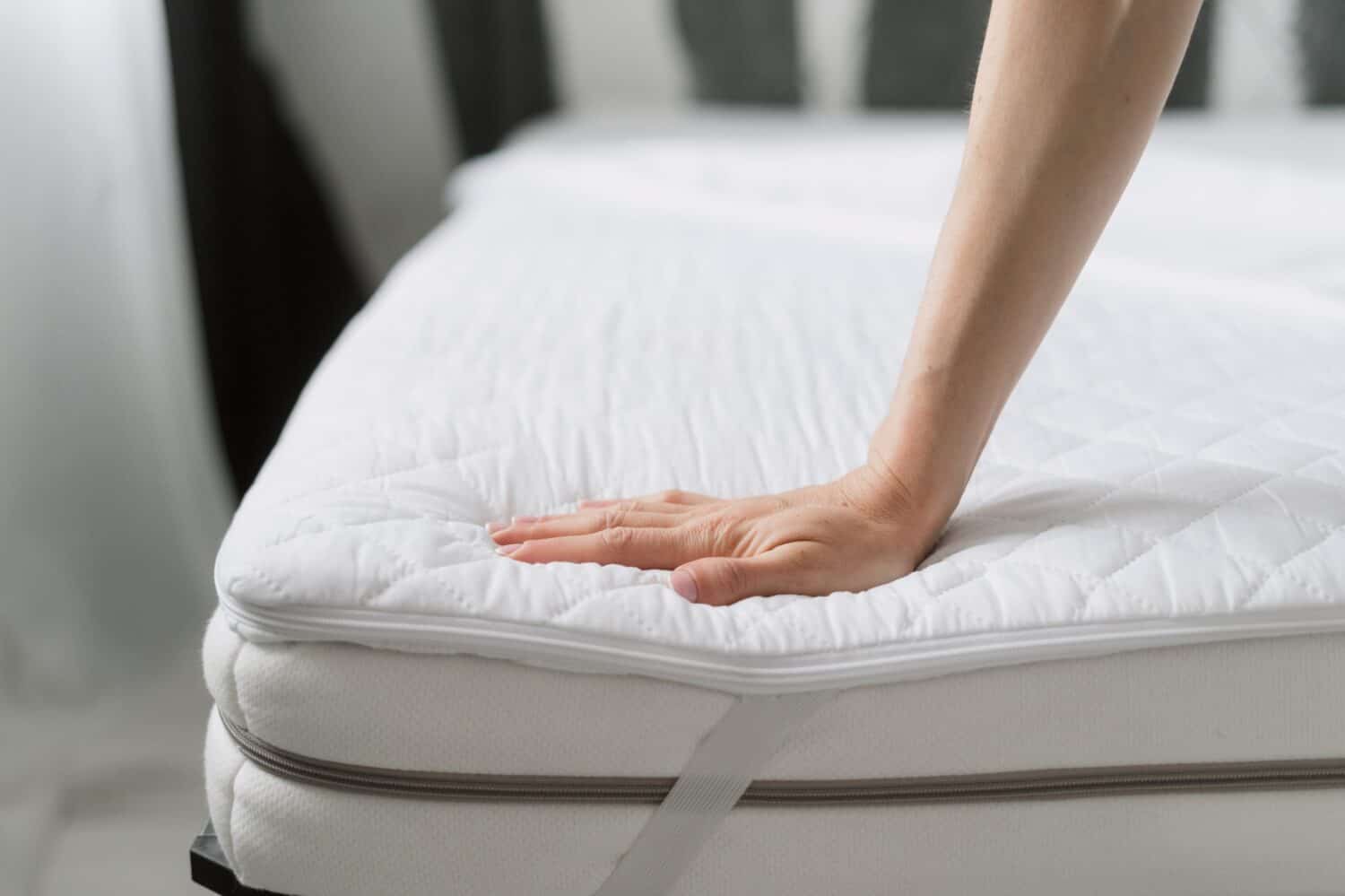 cropped shot of female hands choosing orthopedic memory foam mattress with topper and elastic band on corners on bed at store, protection surface, comfort sleeping concept