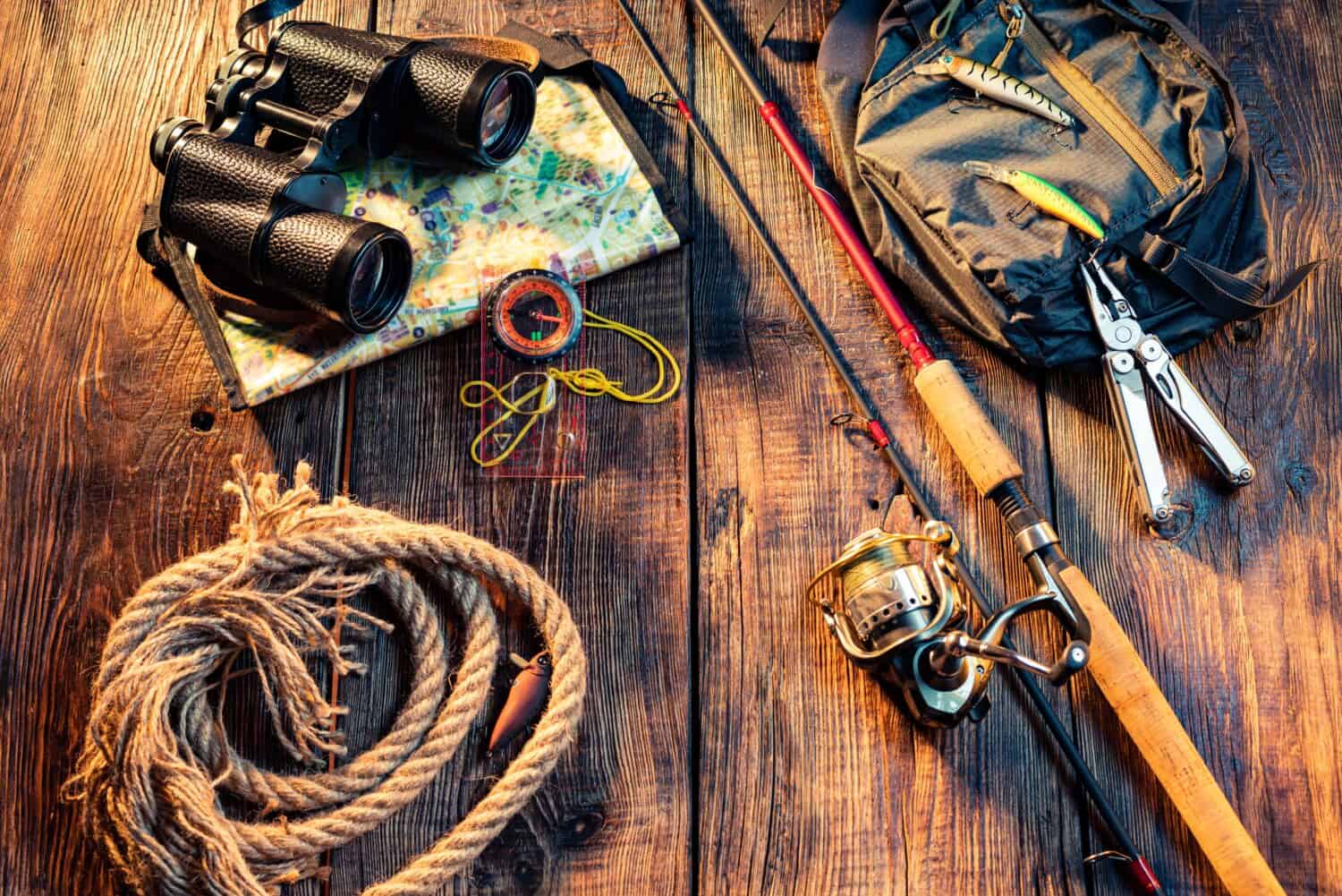 Fishing spinning with a reel line. Fishing items on a wooden background. Binoculars and rope. Copy space in centre.