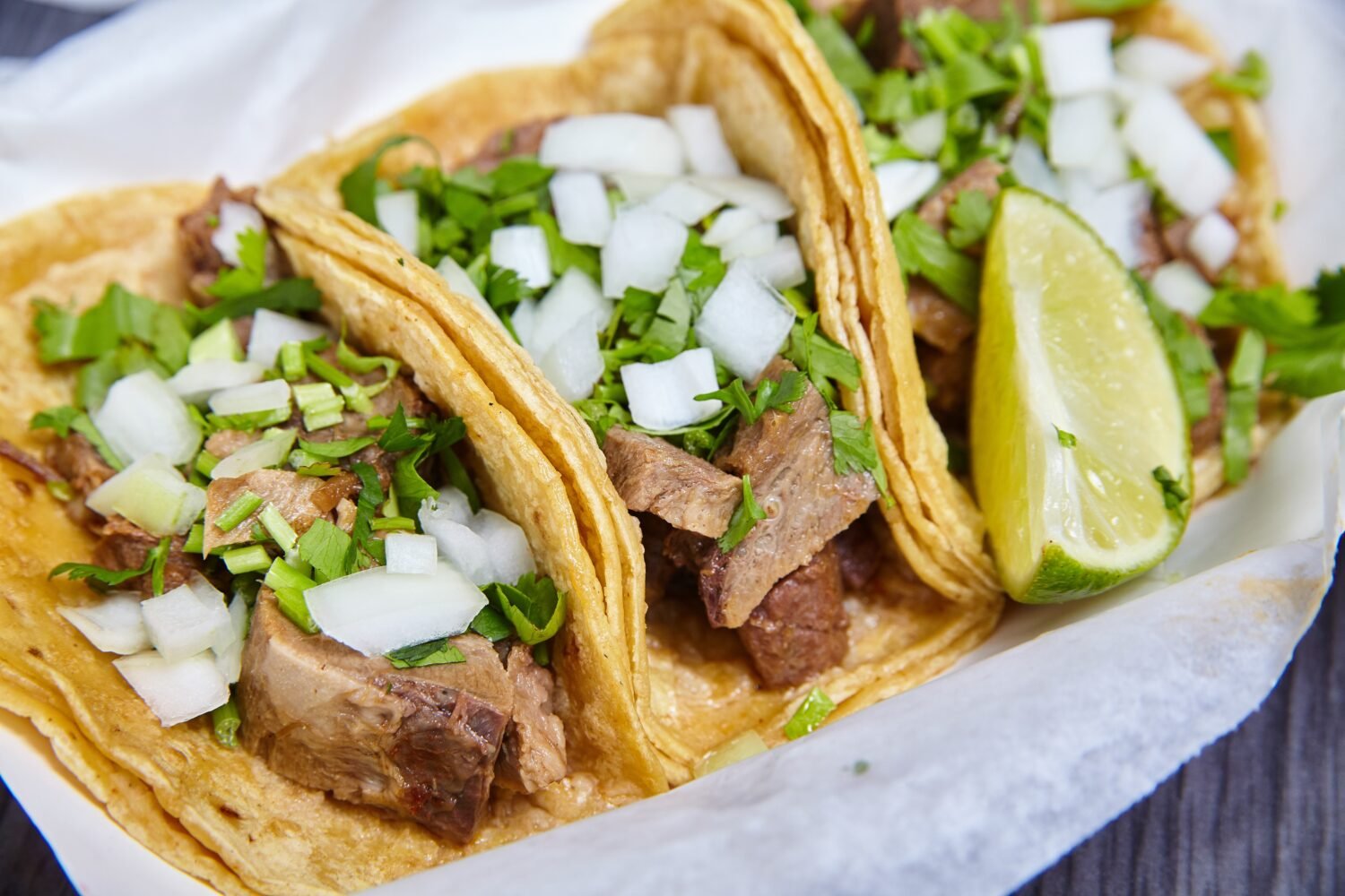Lengua chow beef tongue 3 street tacos Mexican with cilantro, lime wedge, and onions