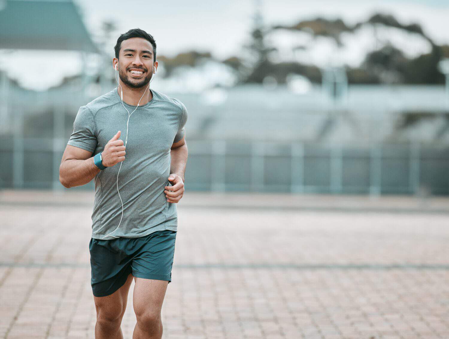 Sports, portrait and male athlete running with earphones for music, radio or podcast for motivation. Fitness, exercise and man runner in outdoor cardio workout routine for race or marathon training.