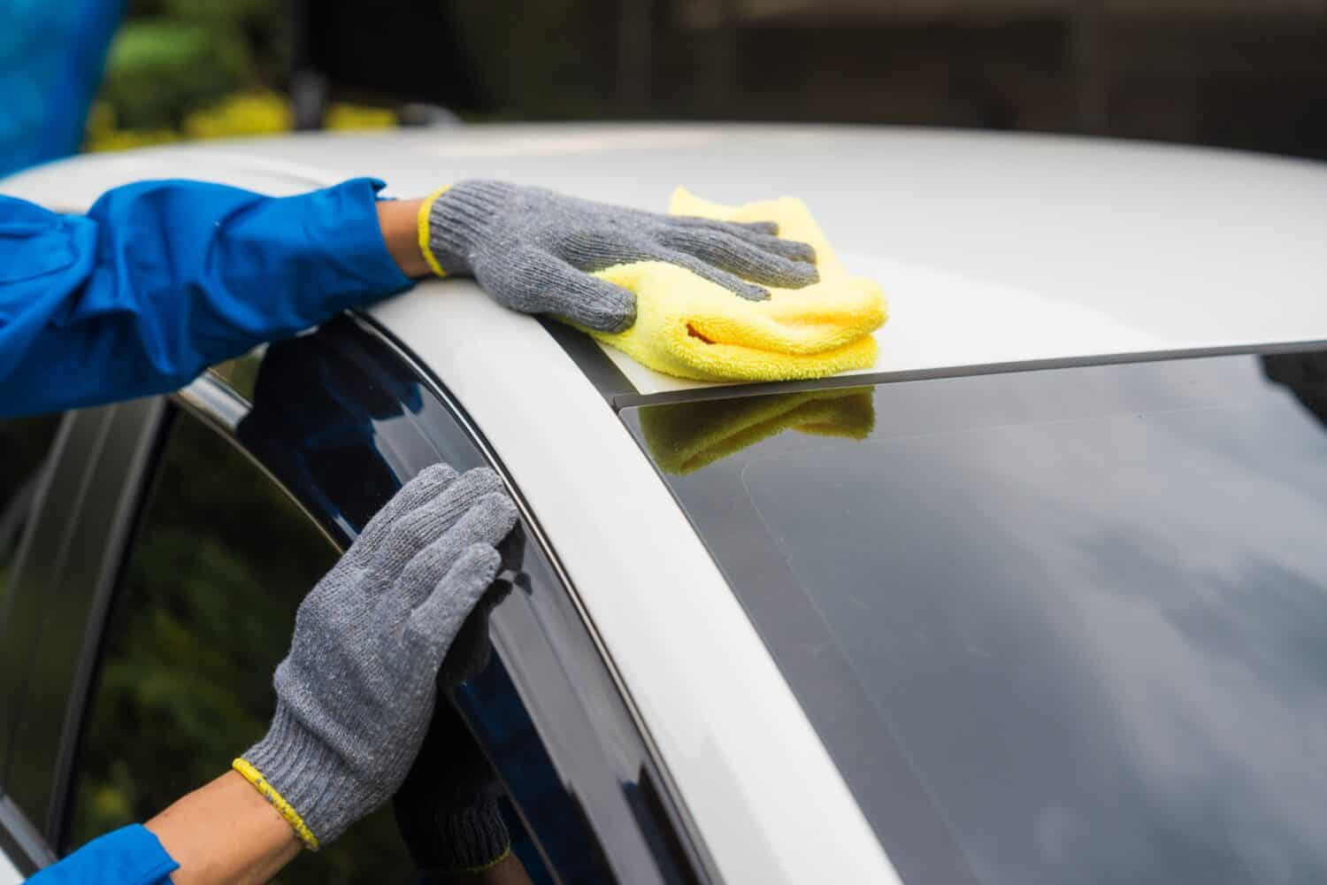 close-up shot of a hand wiping a car's windshield with yellow microfiber cloth, mechanic's hand polishing car hood with soft cloth