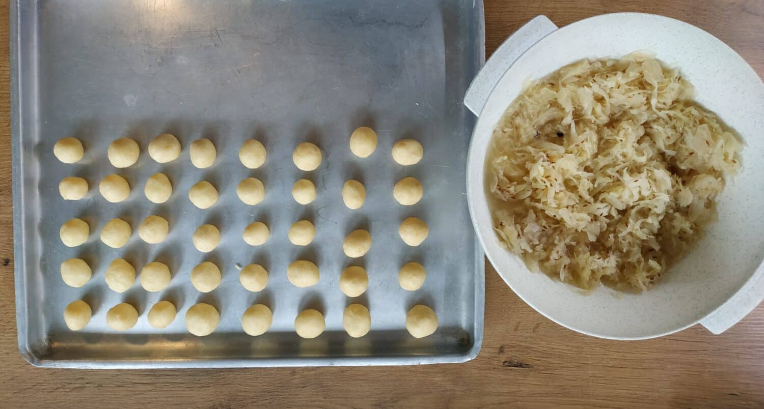 Typical slovakian food potato balls with sauerkraut in process, sauerkraut in white plastic bowl and potato balls at the metal tray at the wooden table.