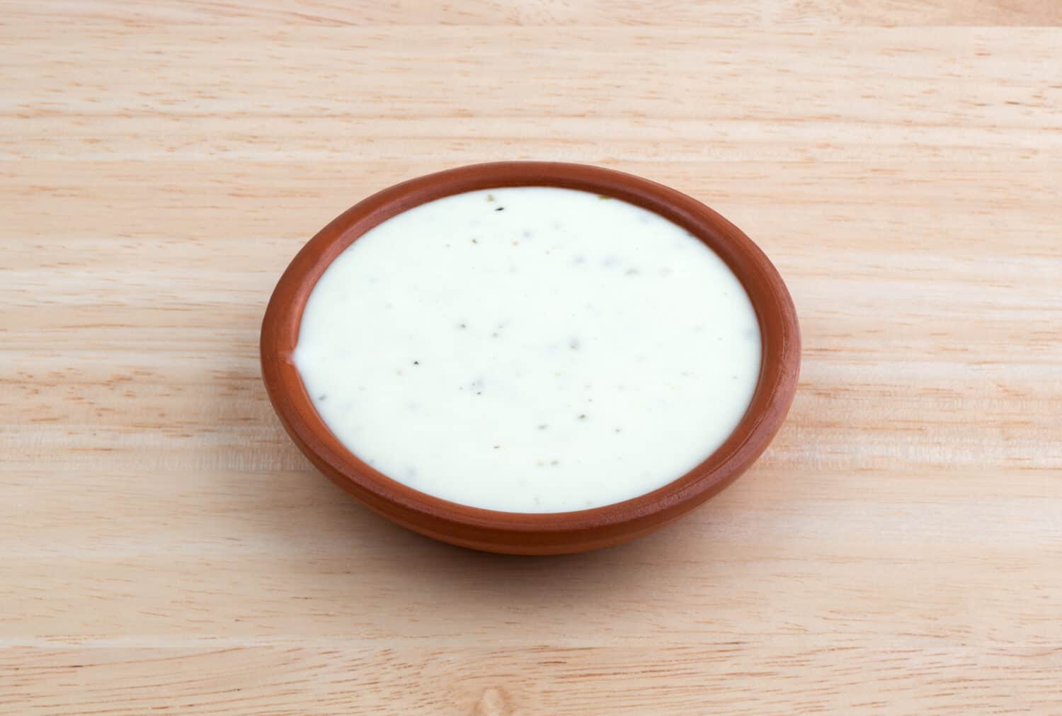 Side view of a small bowl of ranch dressing on a wood table top illuminated with natural light.
