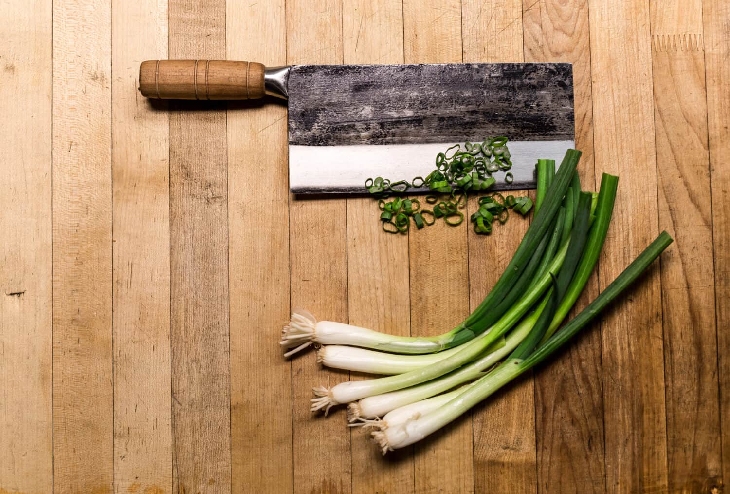 Chinese chopping knife with green onions on a wood cutting board.