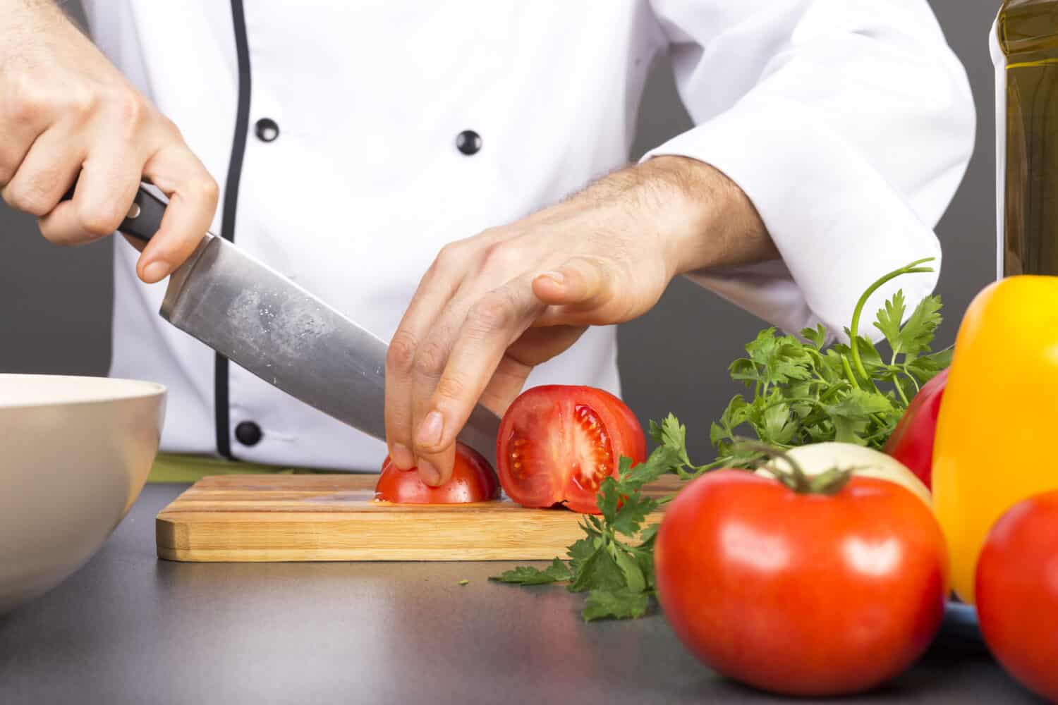 Chef's hands cutting red fresh tomato on a wooden board