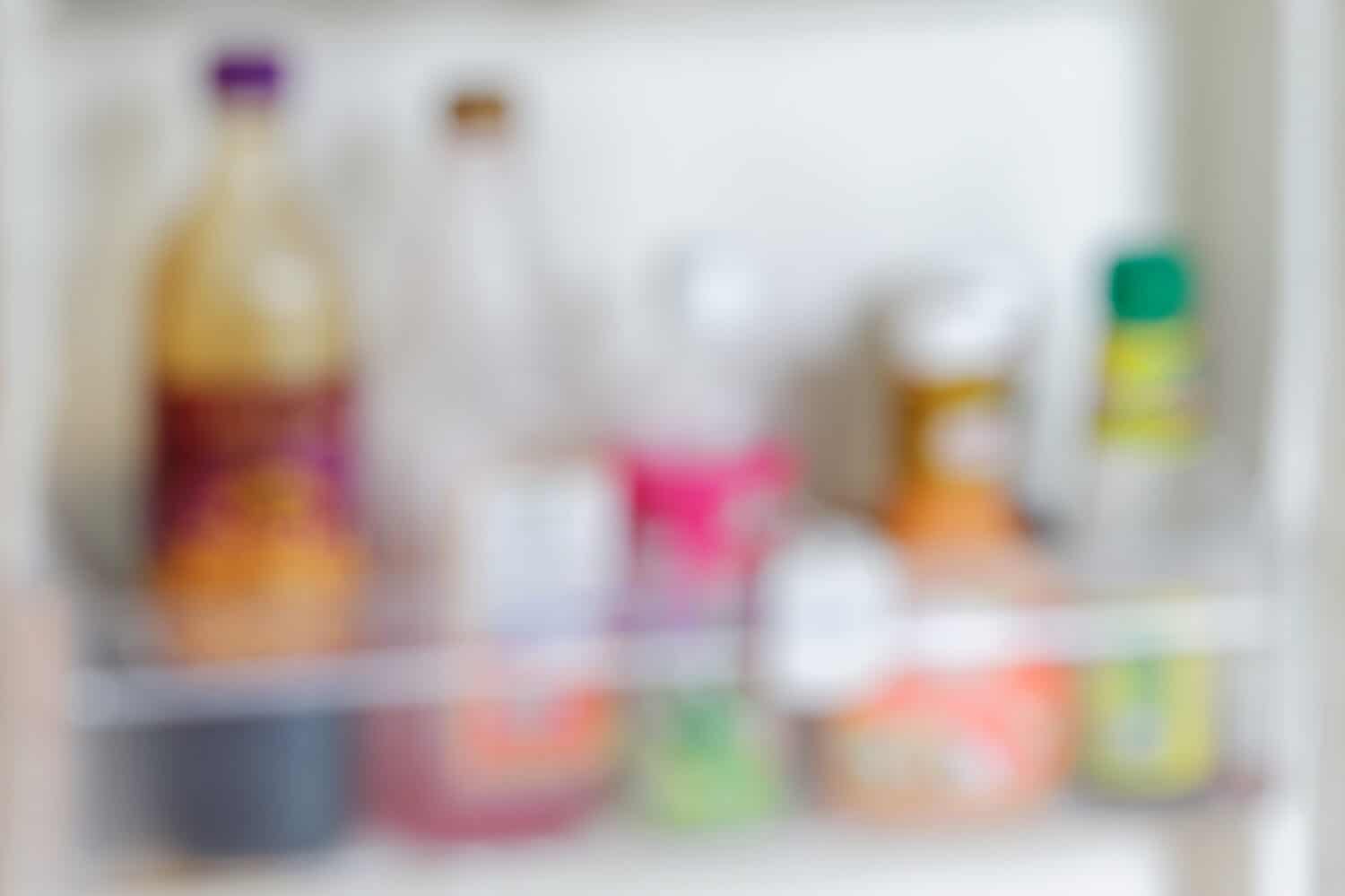 Blurred picture of ketchup, salad dressings, mayonnaise and sauces bottles arranged side by side inside a refrigerator.