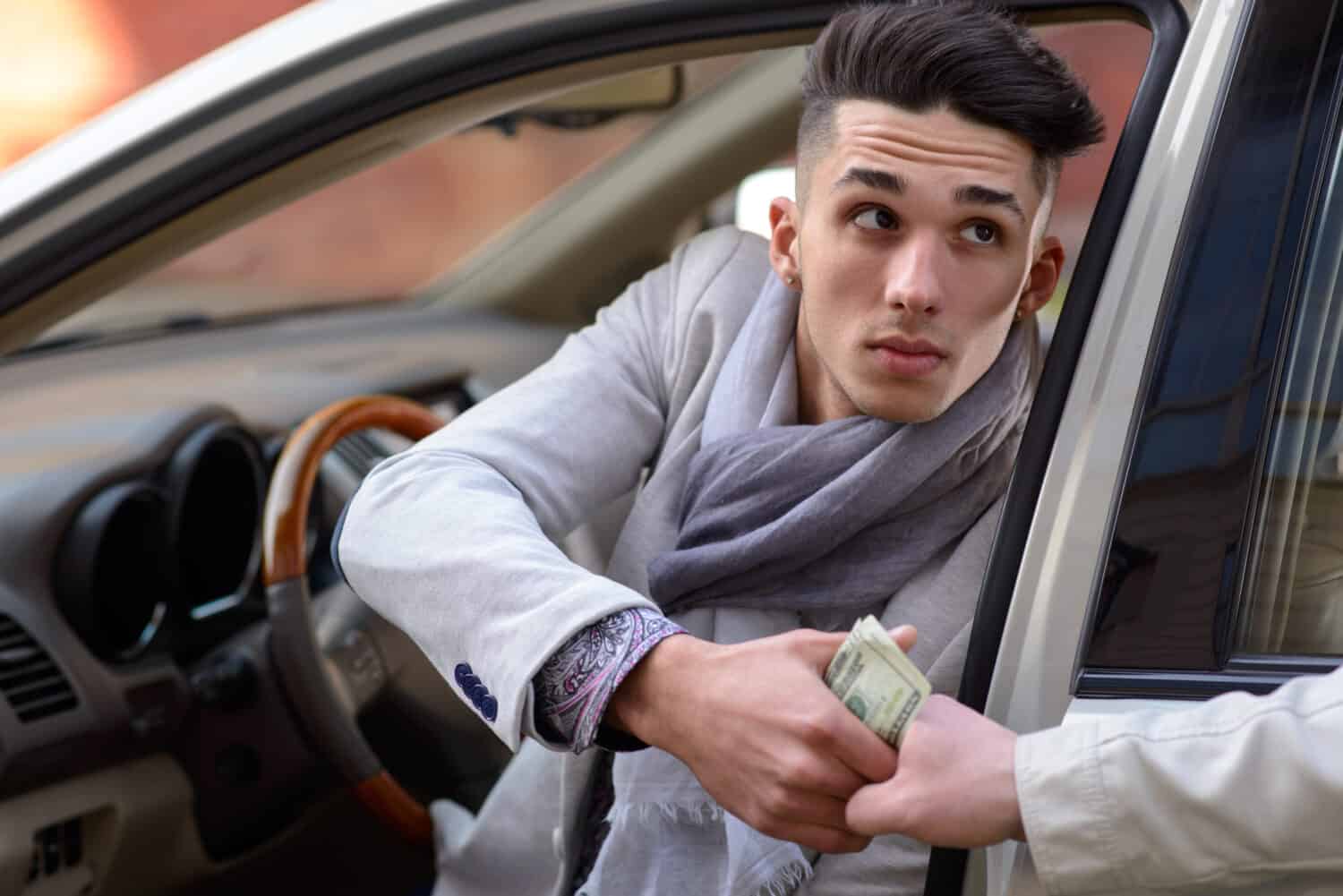 man sitting behind the wheel of the car gives money to another man
