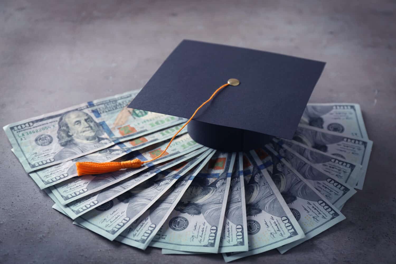 Graduation hat and dollar banknotes on table. Tuition fees concept