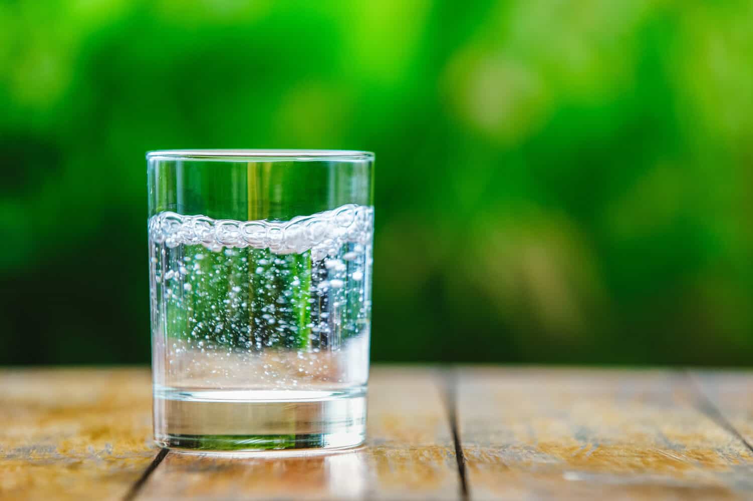 A glass of water on green background. The wooden table. Pure water with gas. Sparkling water
