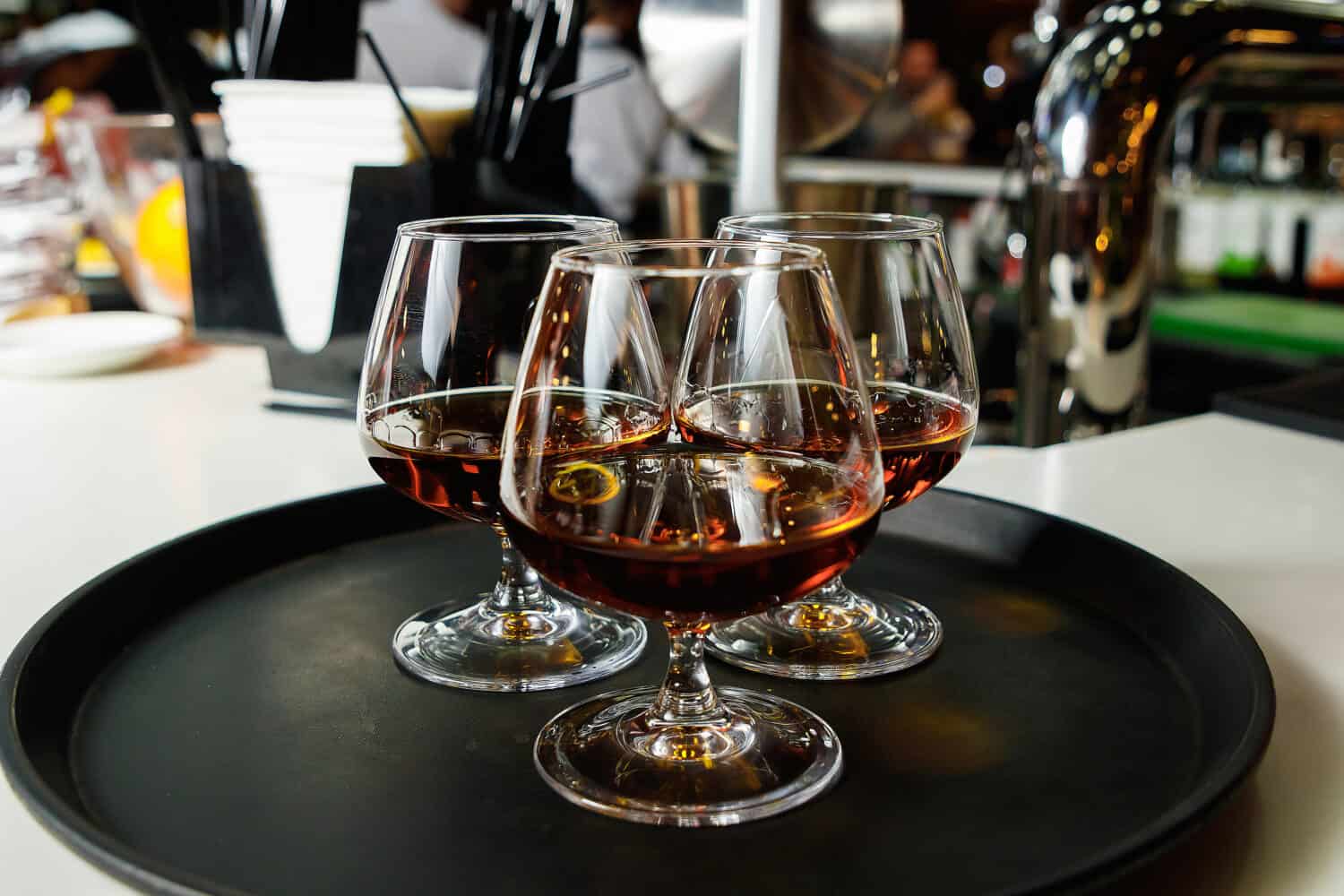 Three glasses with cognac on a dark tray, close-up, service, nightclub.