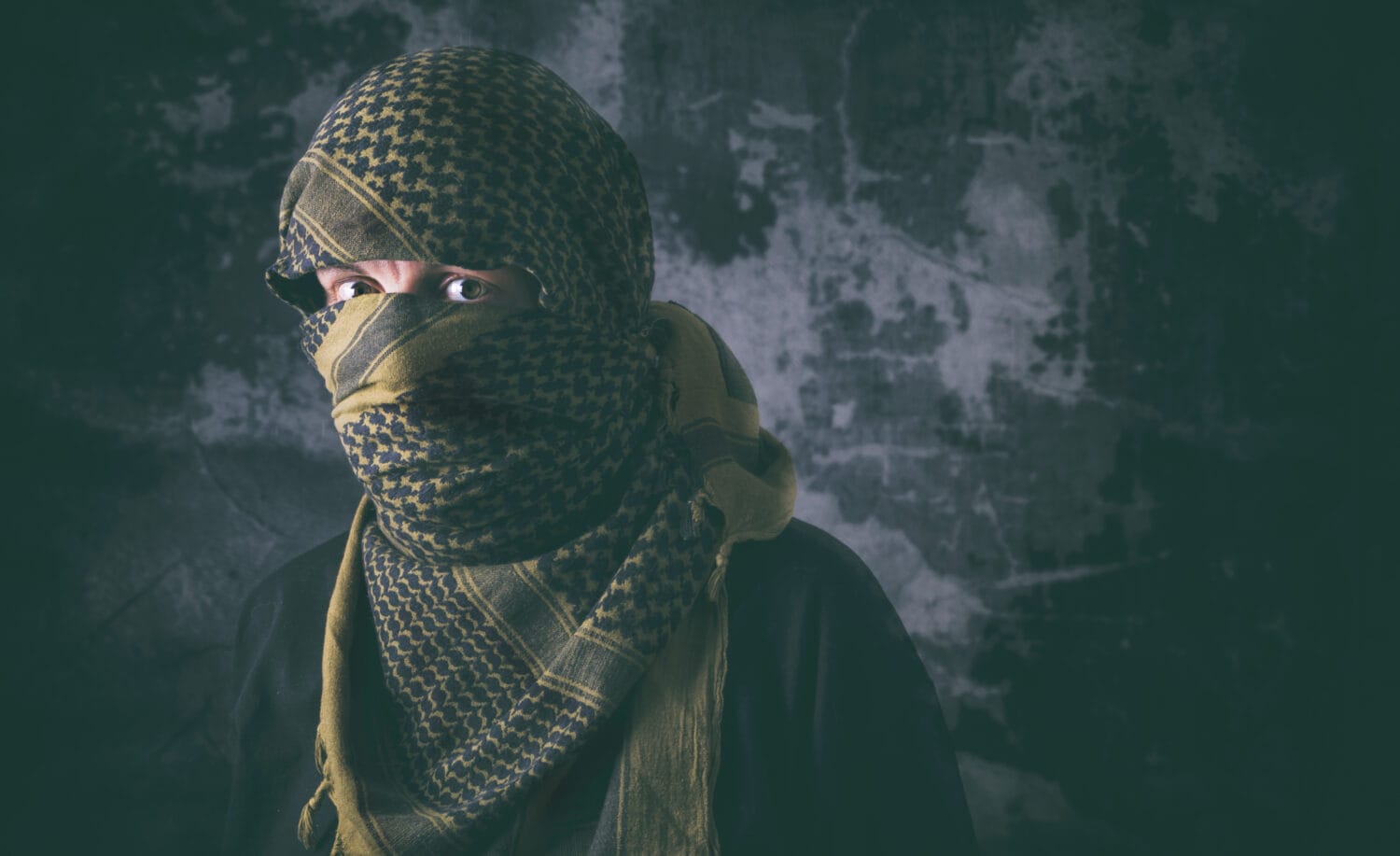 Masked terrorist with tactical Shemagh scarf and treating look with grungy background. Concept of terrorism and violence.