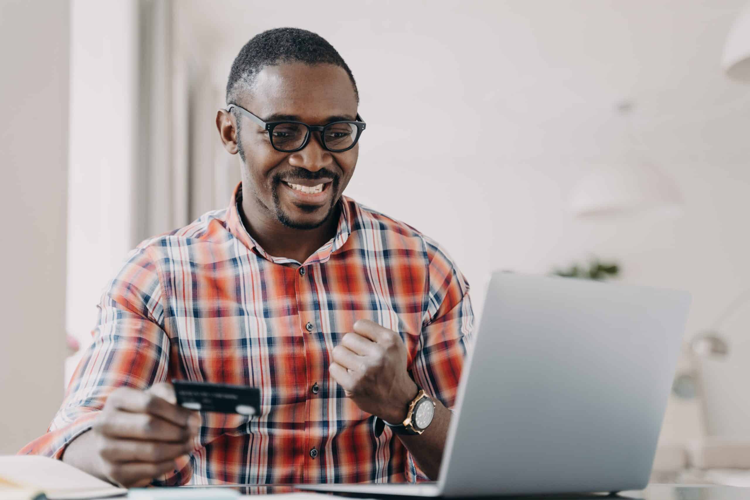 E-banking, e-commerce. African american man holding credit card uses e-bank online service at laptop