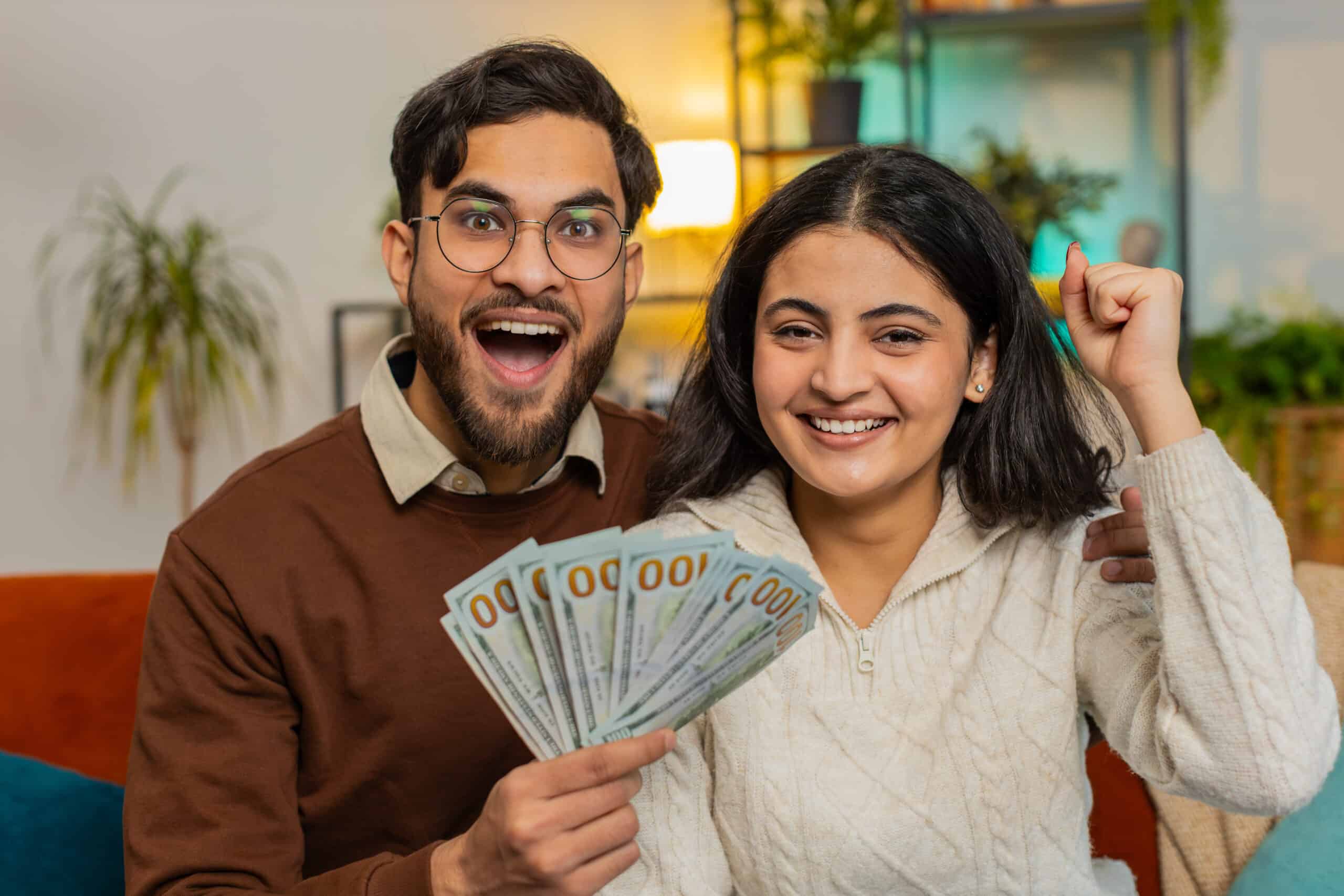 Happy young couple holding showing money cash together and looking at camera celebrate win victory