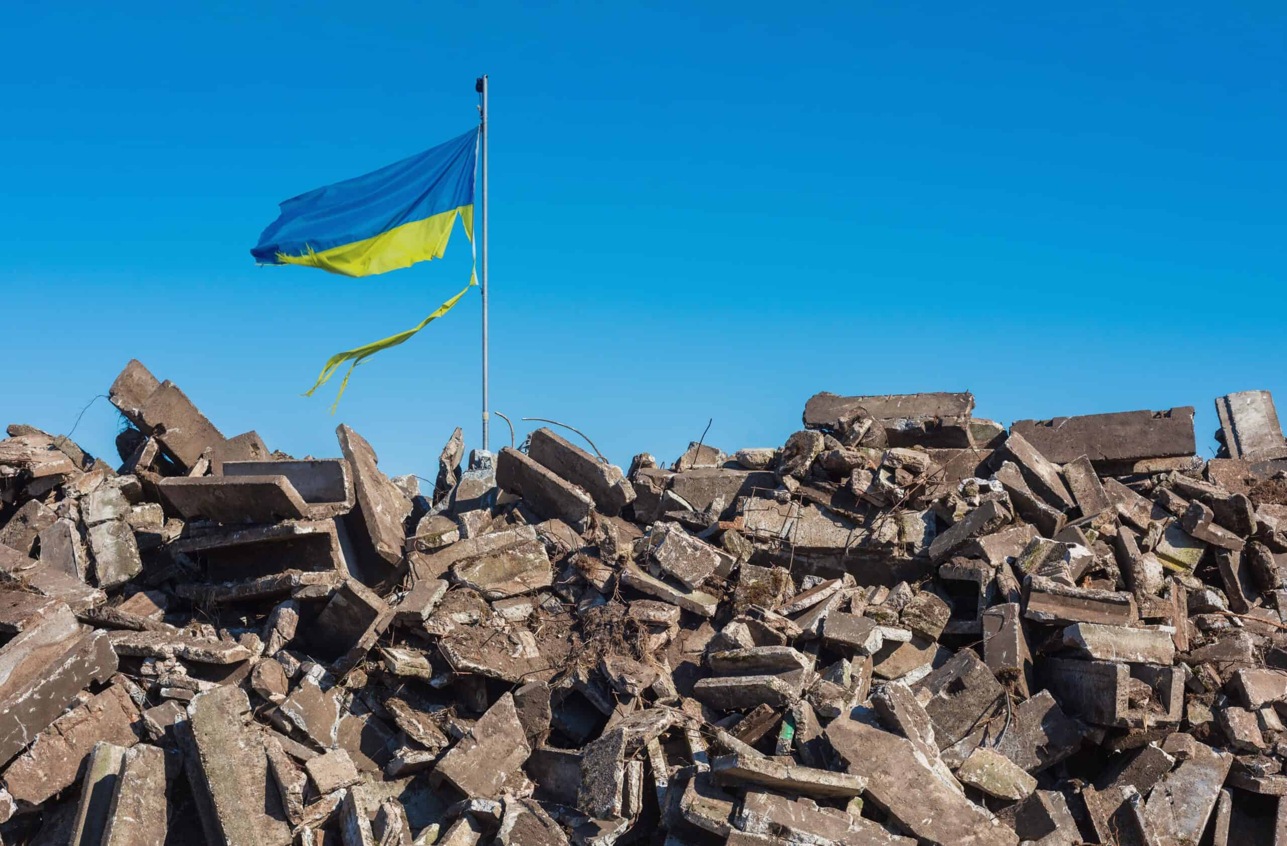 Ukraine | war in ukraine. Destroyed Ukrainian building and damaged flag in the wind.