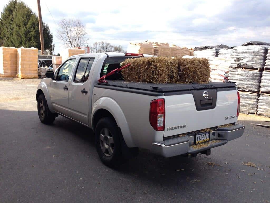 White Nissan Frontier with Black Bed Cover Hauling Hay on Top by DiamondBack Truck Covers