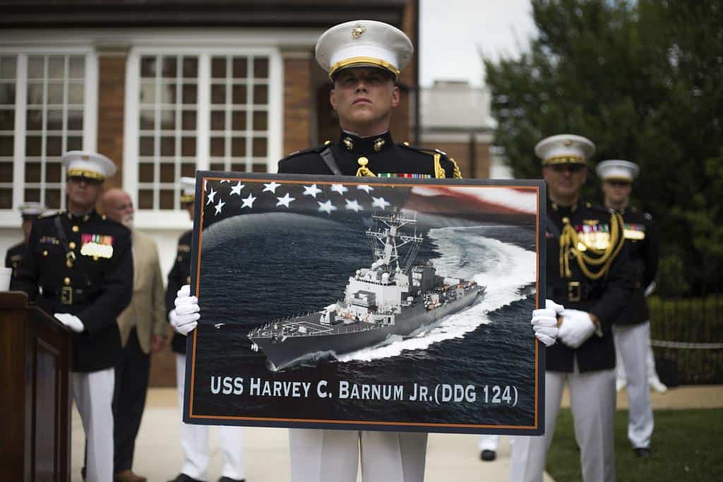 A Marine holds a poster of the future Arleigh Burke-class guided-missile destroyer USS Harvey C. Barnum, Jr. by Official U.S. Navy Imagery