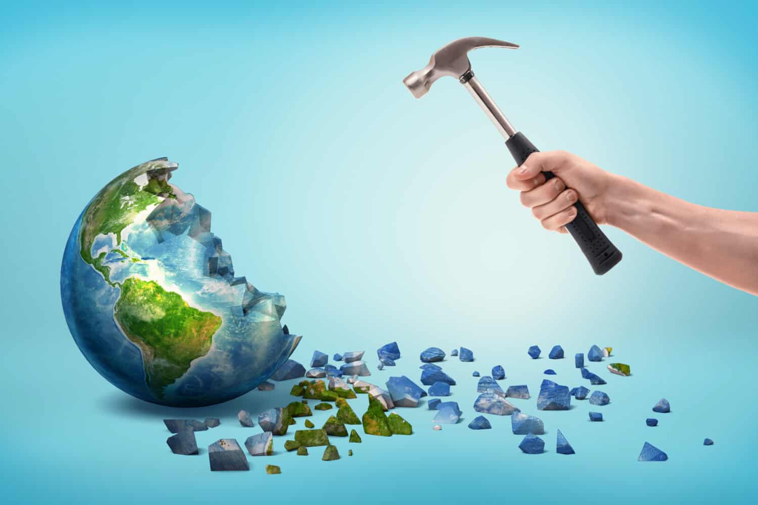 A male hand holds a metal hammer near a semi-broken Earth globe with small pieces fallen out of it. Human vs Earth. Environmental issues. Destroying the Earth.