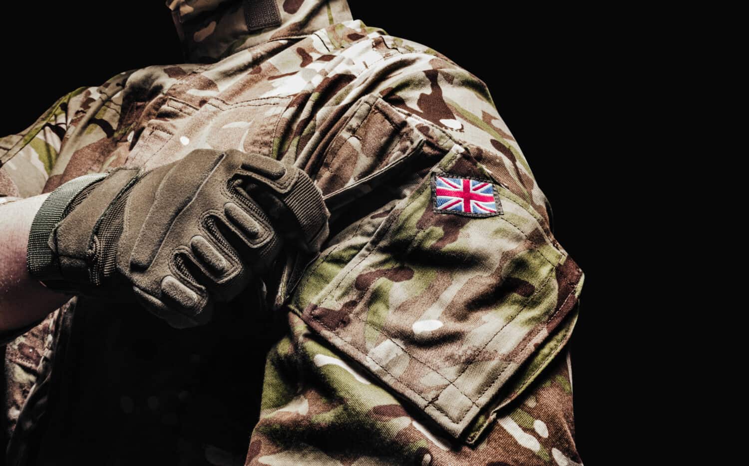 Photo of a british soldier in multicam camouflage tunic using pocket on black background.
