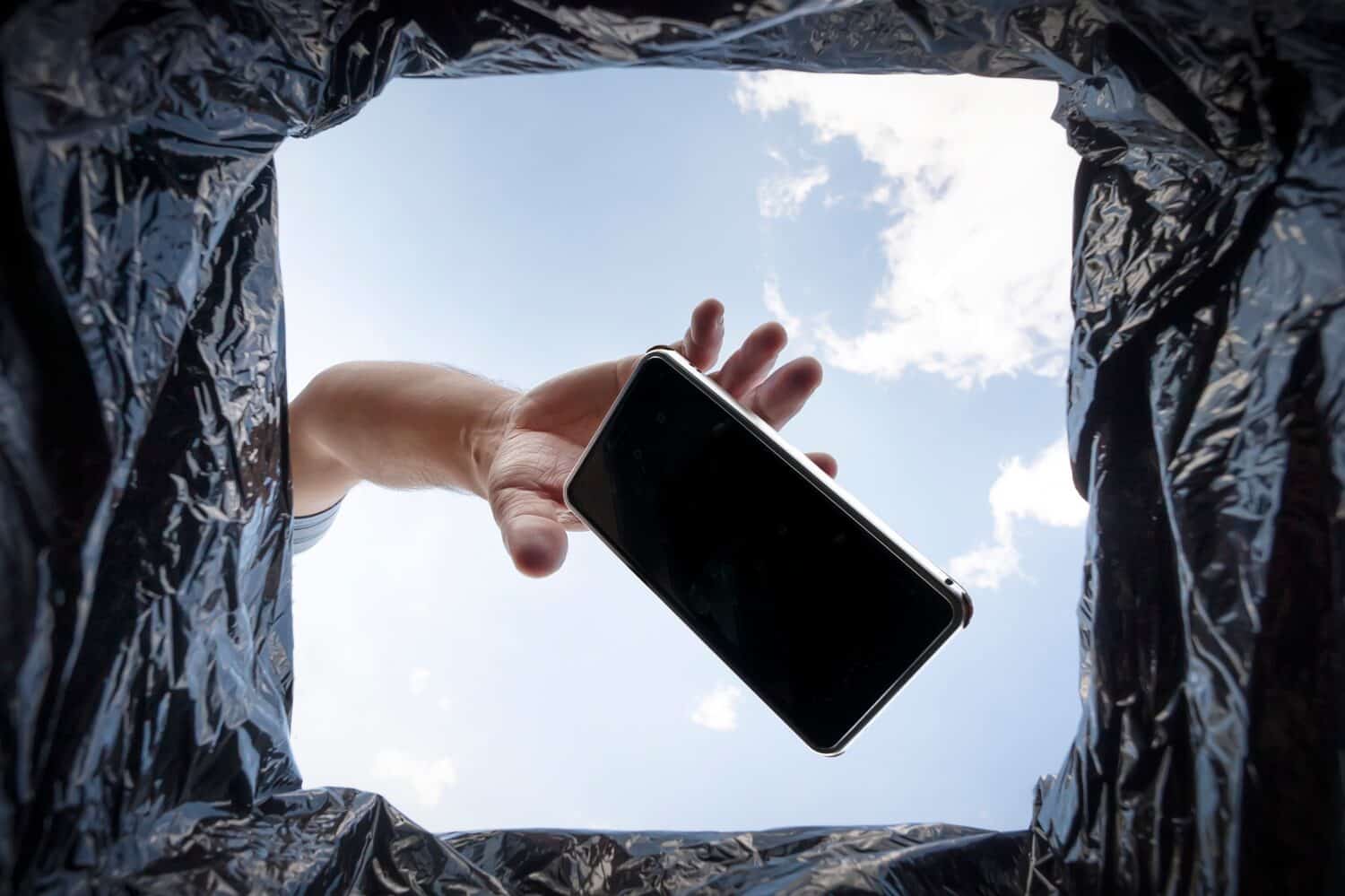 a man throws a non-working smartphone into a trash can. Bottom view from the trash can. The problem of recycling and pollution of the planet with garbage.