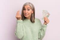 middle age woman making capice or money gesture, telling you to pay. dollar banknotes concept